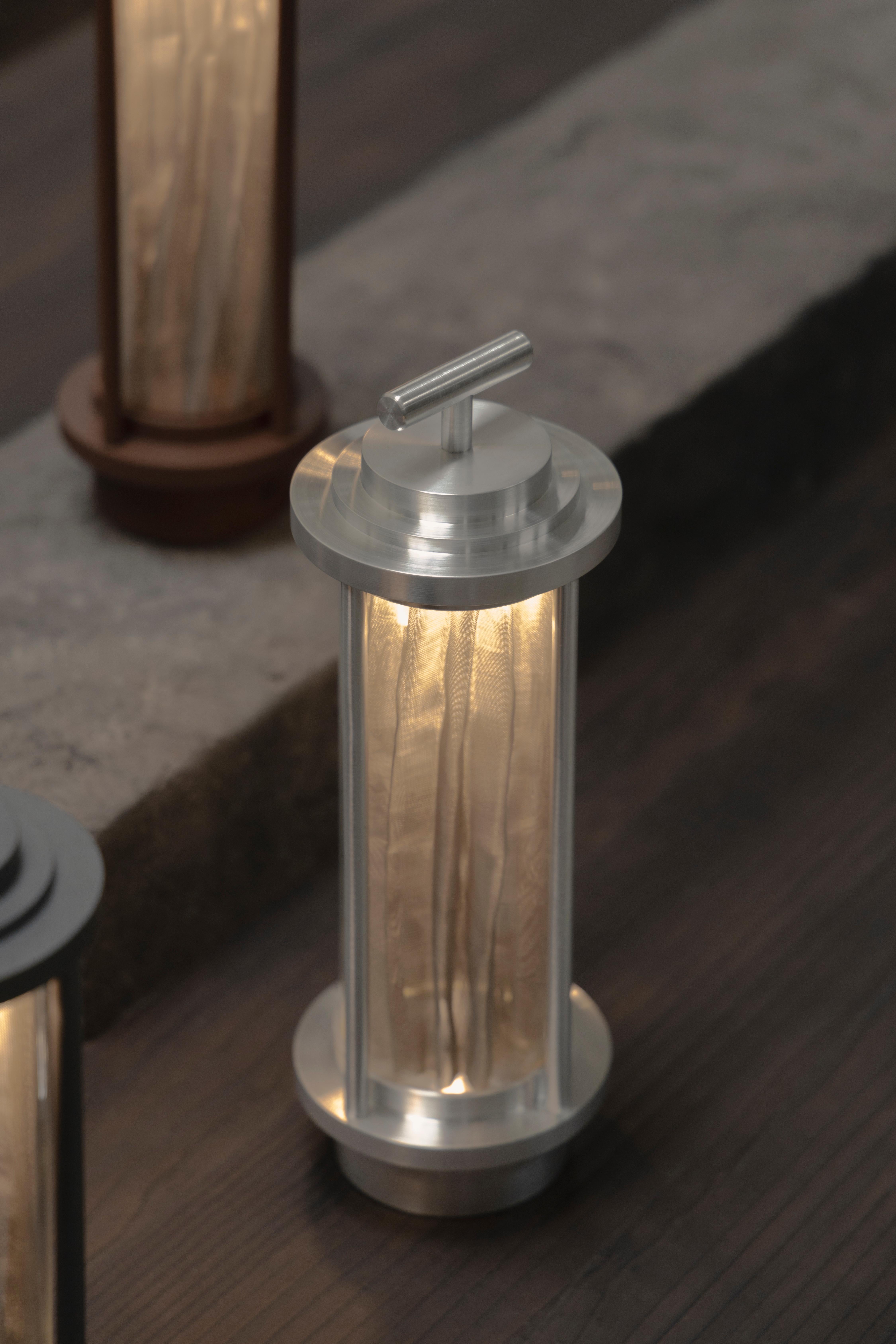 Nòmada Portable & Rechargeable Table Light with Steel Mesh by Nuumbra
Dimensions: Ø 10 x H 30 cm. 
Materials: Steel mesh and brushed aluminum.

Available in brushed aluminum or in a powder-coated finish. Prices may vary. All our lamps can be wired