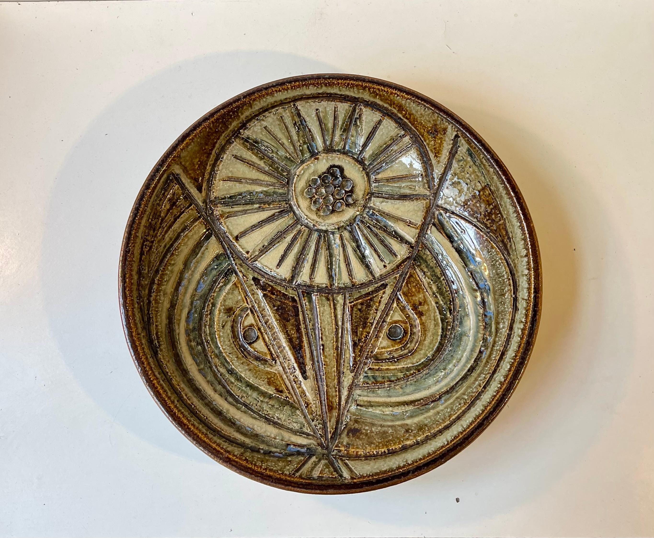 Large handmade centerpiece bowl or dish featuring a variety of earthy glazes set in an abstract sunflower looking motif. It was designed by female ceramist Noomi Backhausen in the late 1960s and manufactured by Soholm. The Bowl is fully marked to
