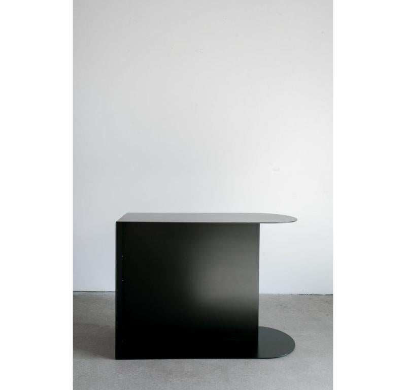 La table d'appoint Norah offre un mélange unique de forme et de fonctionnalité, avec un corps en acier, un plateau et une base en forme de demi-lune qui adoucissent le profil épuré de la pièce. Les deux options de plateau - acier ou cuir -