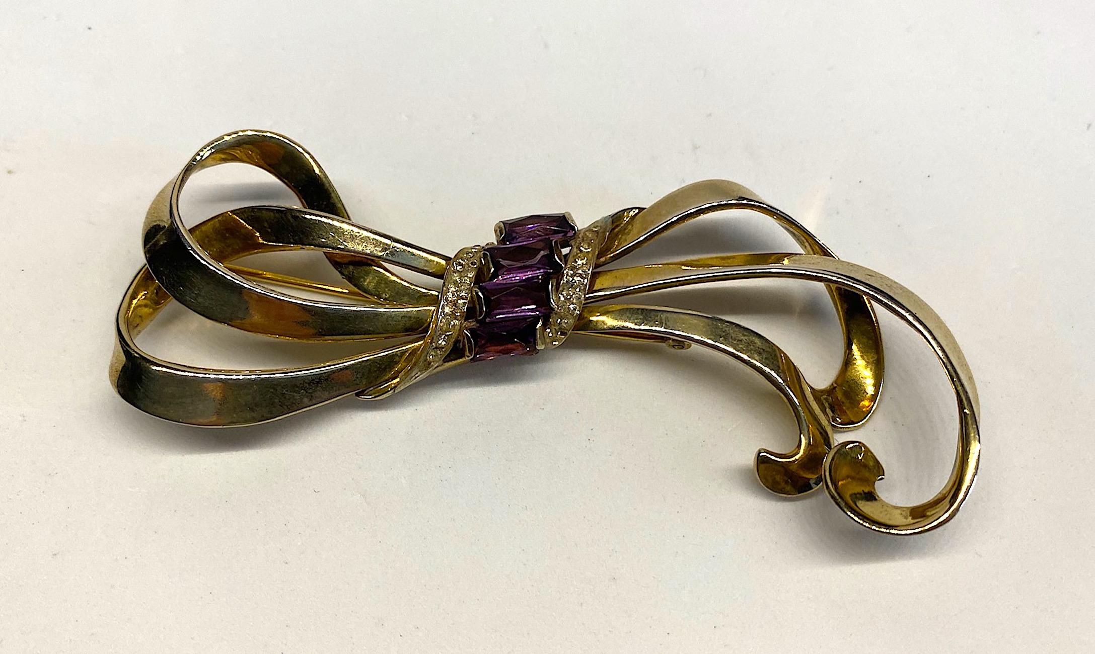 A wonderful sterling silver 1940s large brooch by Nordic Silver Co. Inc. of New York. The brooch is a lovely vintage design of wrapped and looped ribbon in gold on sterling silver vermeil. The center has four vertically set purple faceted crystal