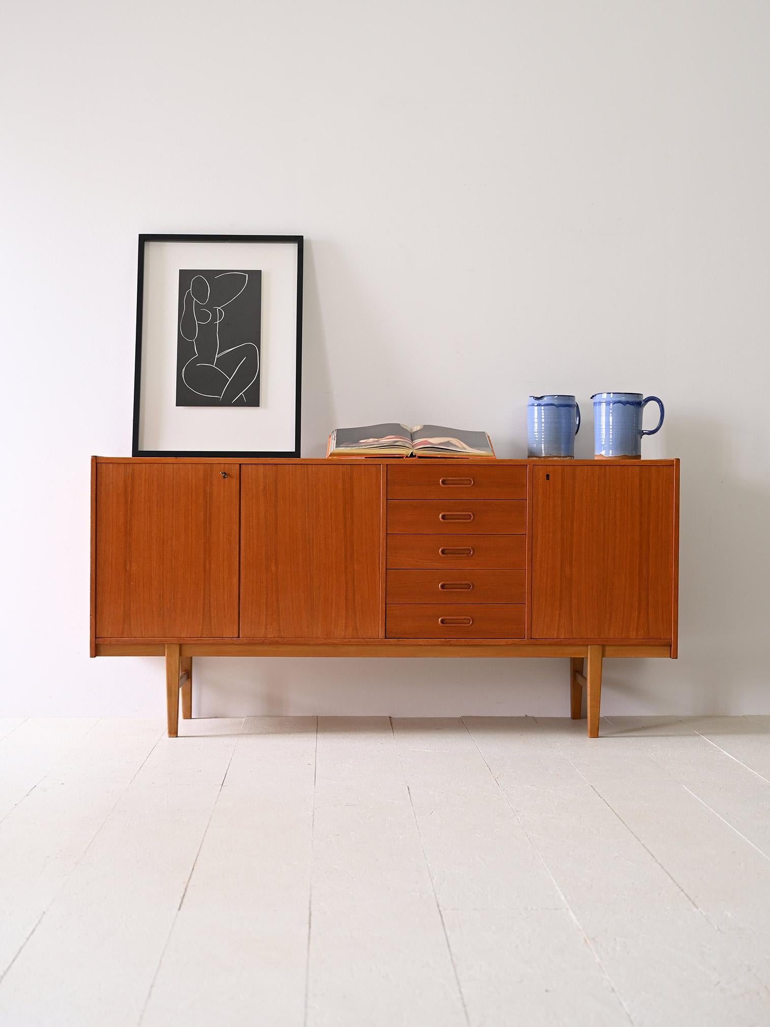 Scandinavian manufactured teak sideboard from the 1950s.

Elegance and quality for this design piece with unmistakable Nordic lines. 

It consists of three hinged doors and five drawers.

The two compartments on either side have a shelf.

Good