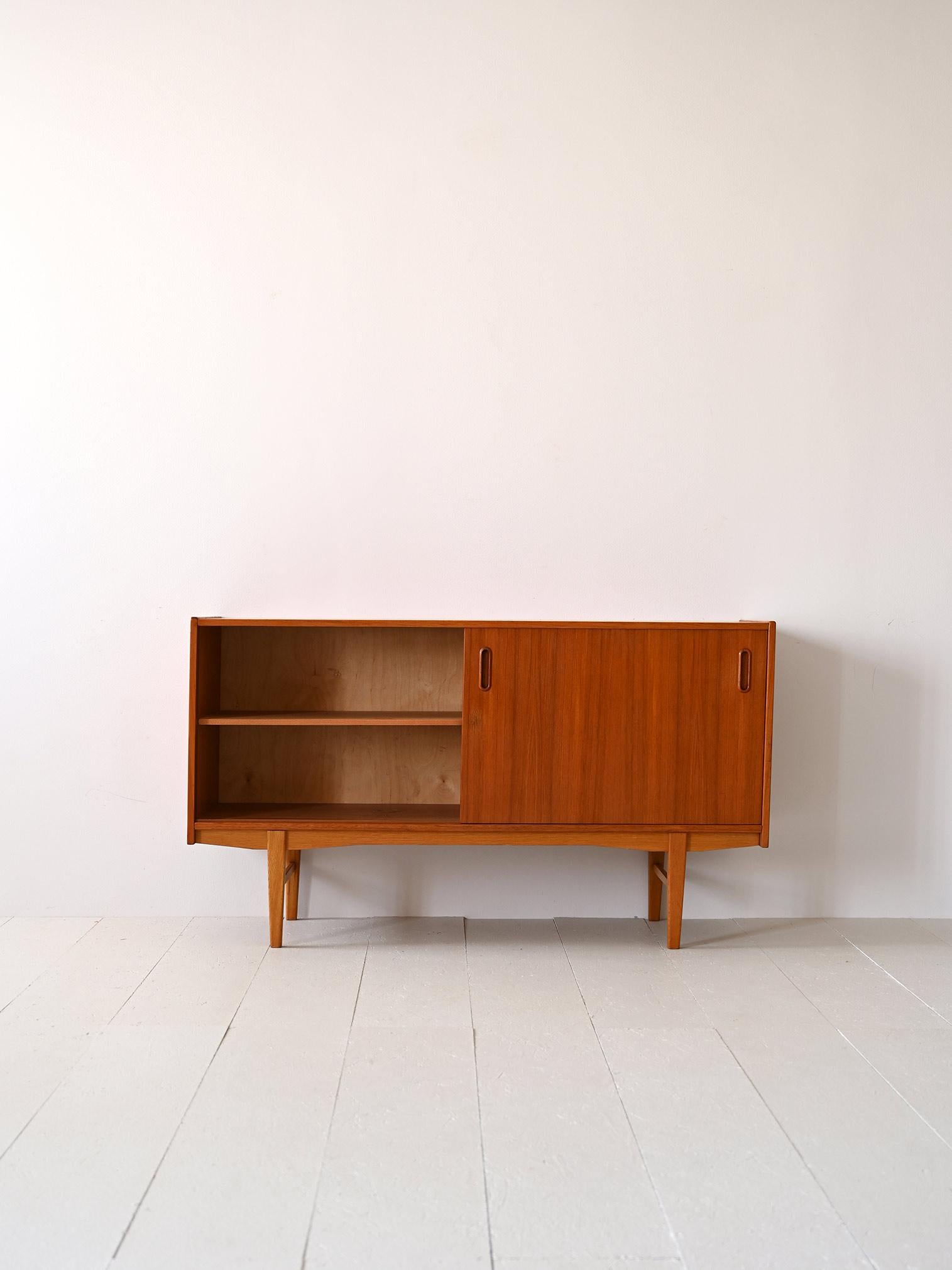 Scandinavian 1960s sideboard in teak and oak.

This cabinet with modern lines consists of 5 drawers on one side and a compartment with a sliding door on the other. Inside is a shelf that divides the space. The handle of the drawers and door is
