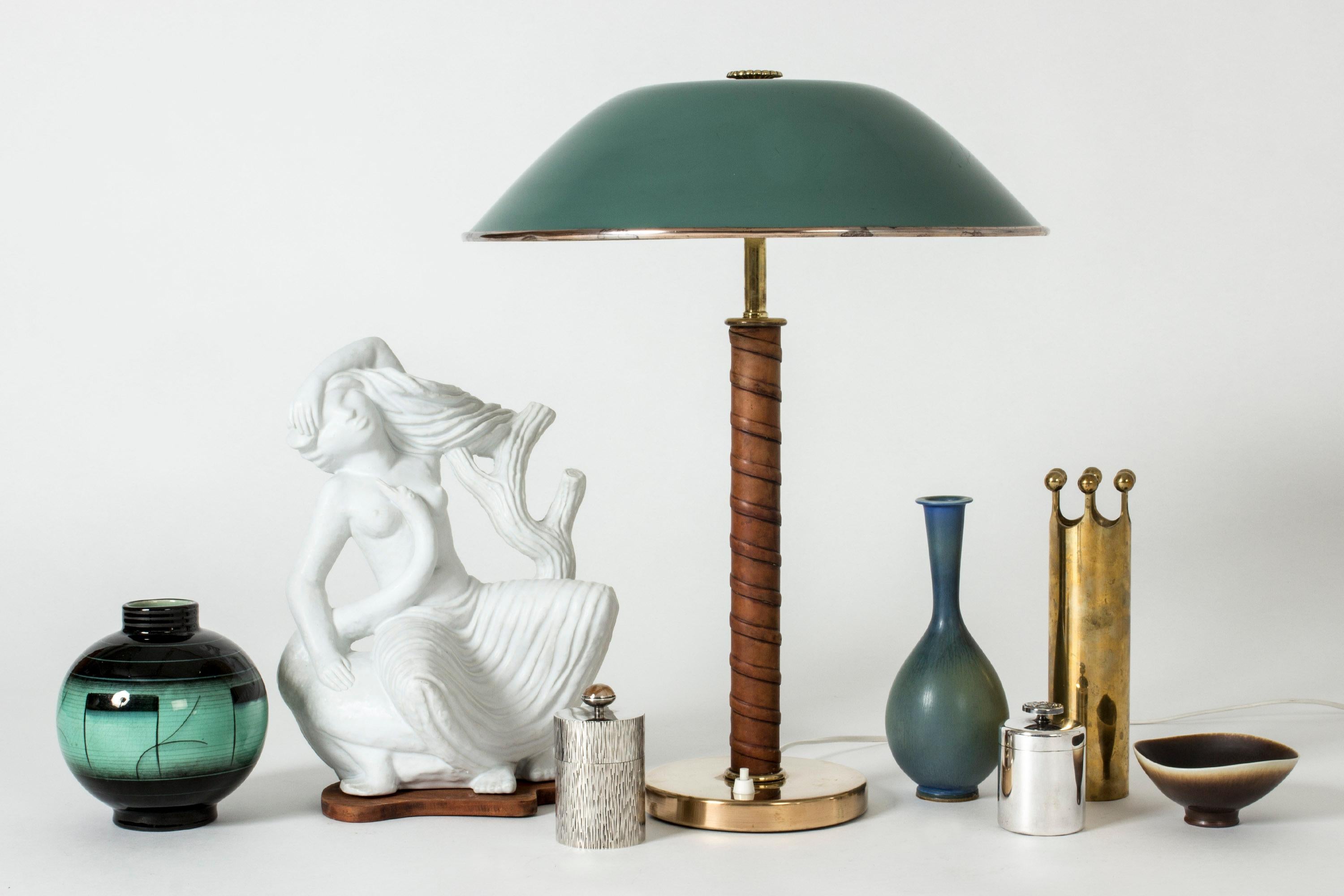 Amazing brass table lamp, with a large green lacquered shade adorned with a brass flower on top. Handle wound with brown leather. Beautiful combination of materials and colors.