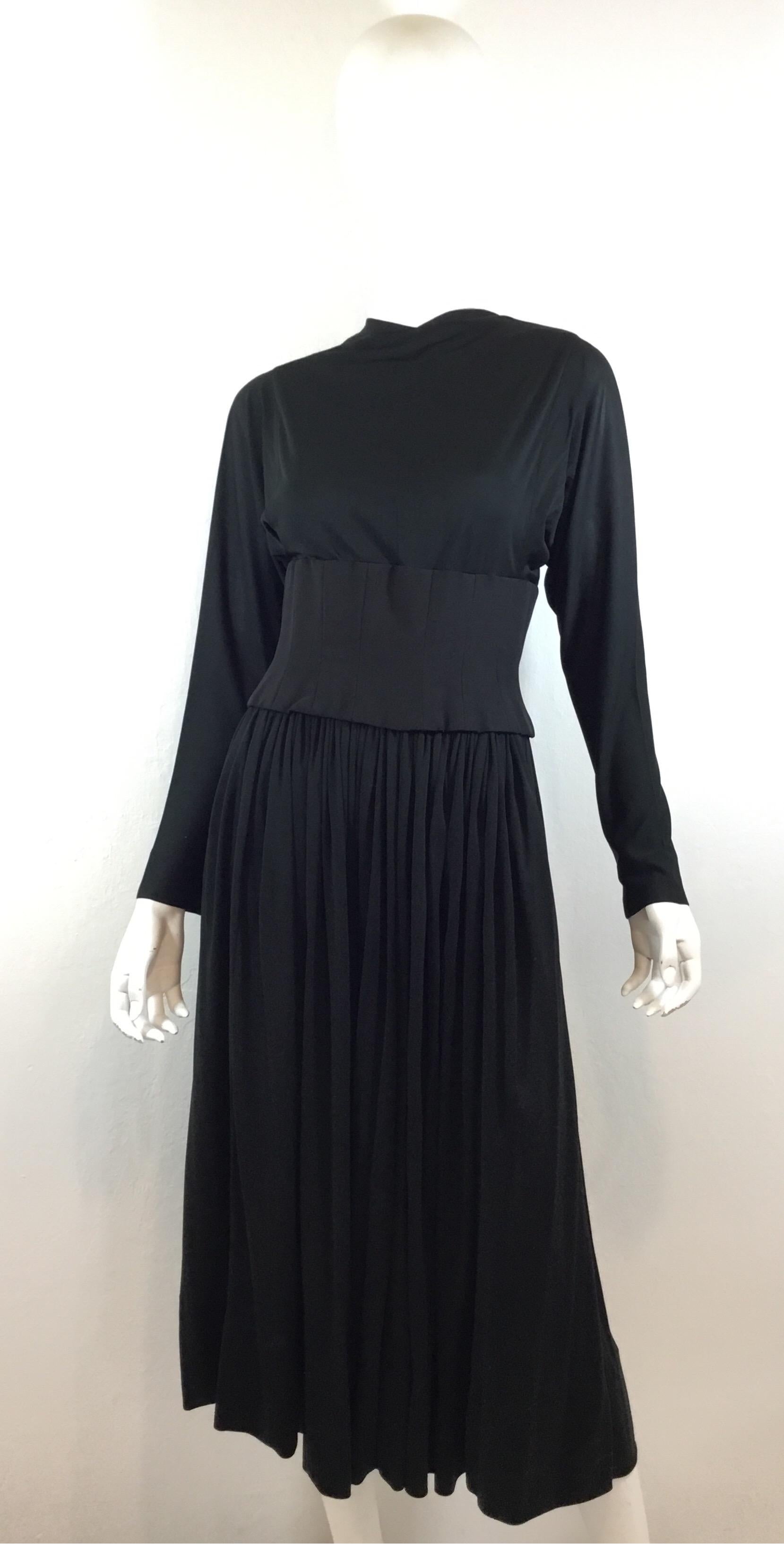 Norman Norell vintage 1940s black matte jersey blouse and skirt set. Blouse has a laced attached boned and corseted faille corset waistband and dolman cut sleeves. Skirt has a side metal zipper and hook fastening with a sweeping hem. Skirt and