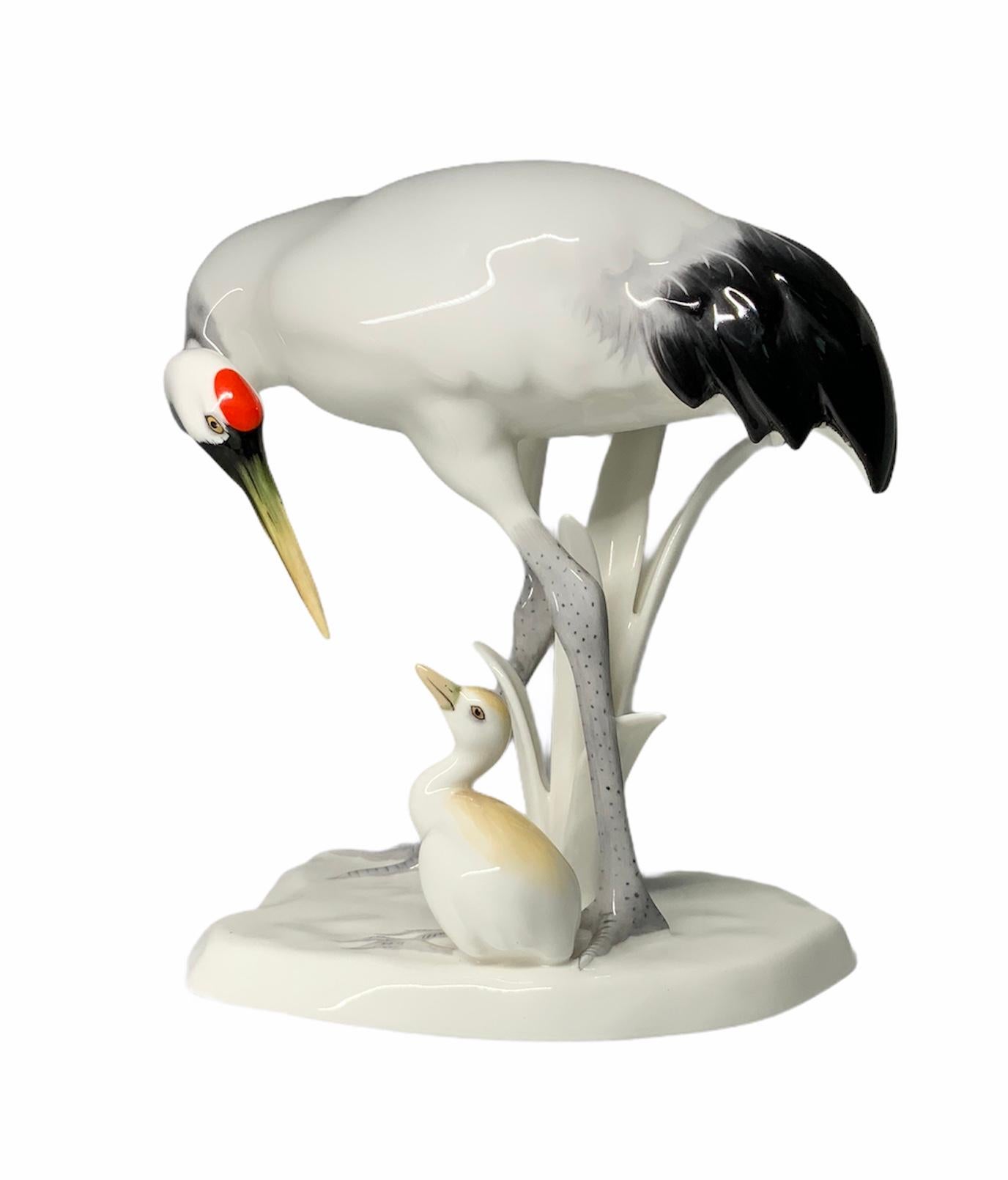 This is a Noritake porcelain of a mother crane bending over its neck and “talking”to his baby crane. Mother crane is hand painted white with black feathers, and also having a red spot in her head. She has also long grey legs. Baby crane is white