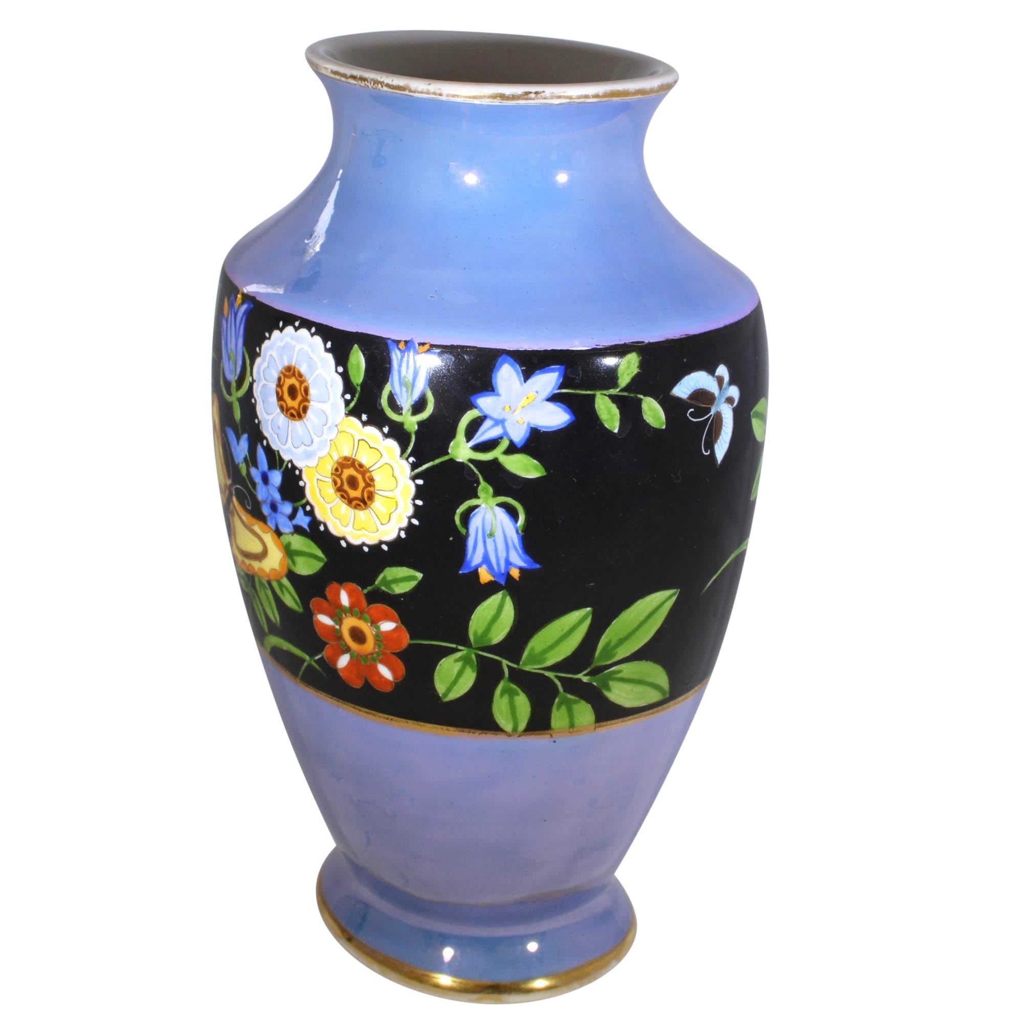 Blue vase had a large black band around the body which is adorned with a whimsical hand painted design of flowers and butterflies. The design has vibrant pinks, reds and many other colors. The design continues around the vase. The gold accents makes