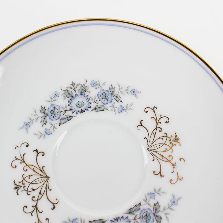 A pretty porcelain white saucer with blue and gold detail by Noritake. This beautiful plate has a painted blue and gold rim with sprays of flowers in varying hues of blue at the center. Two gold decorative flourishes adorn the dish in between the