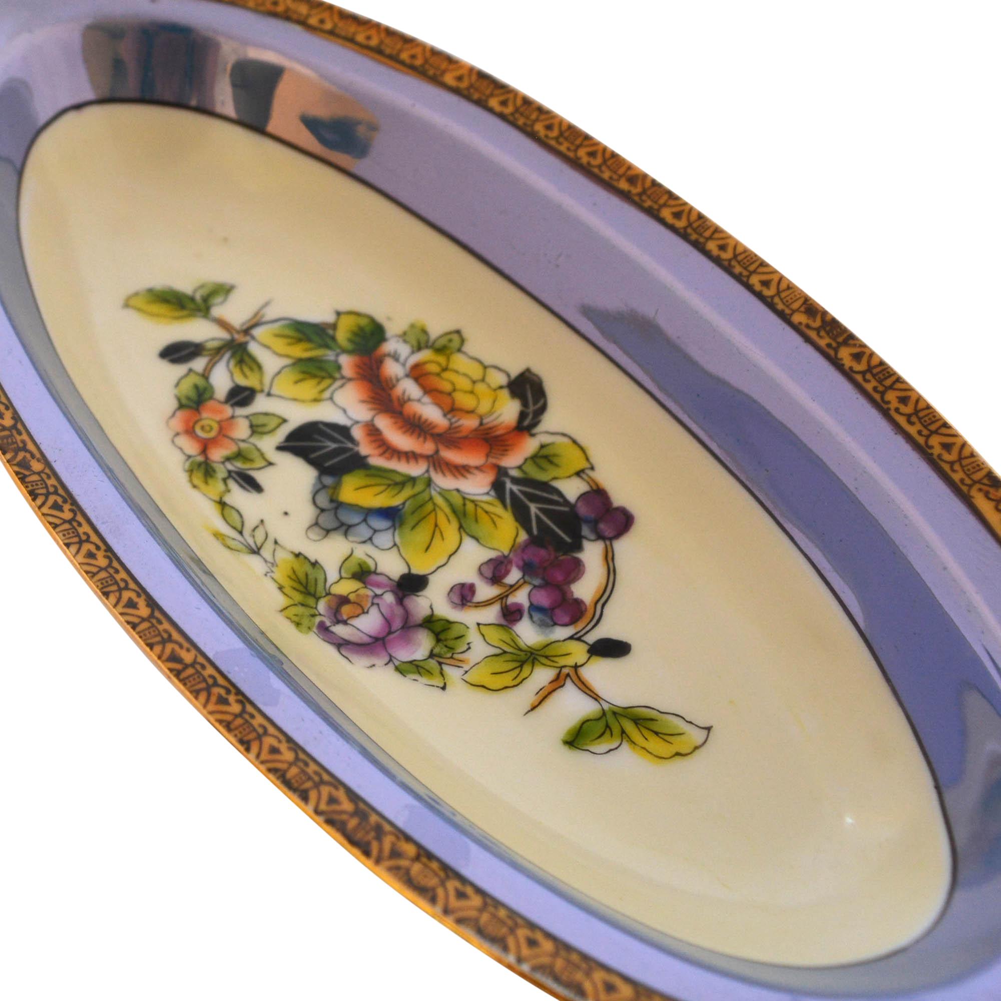 Beautifully hand painted oblong bowl by Noritake features a floral center design. The base of the bowl is a cornflower blue with many other colors such as green, yellow and purple incorporated into the design.