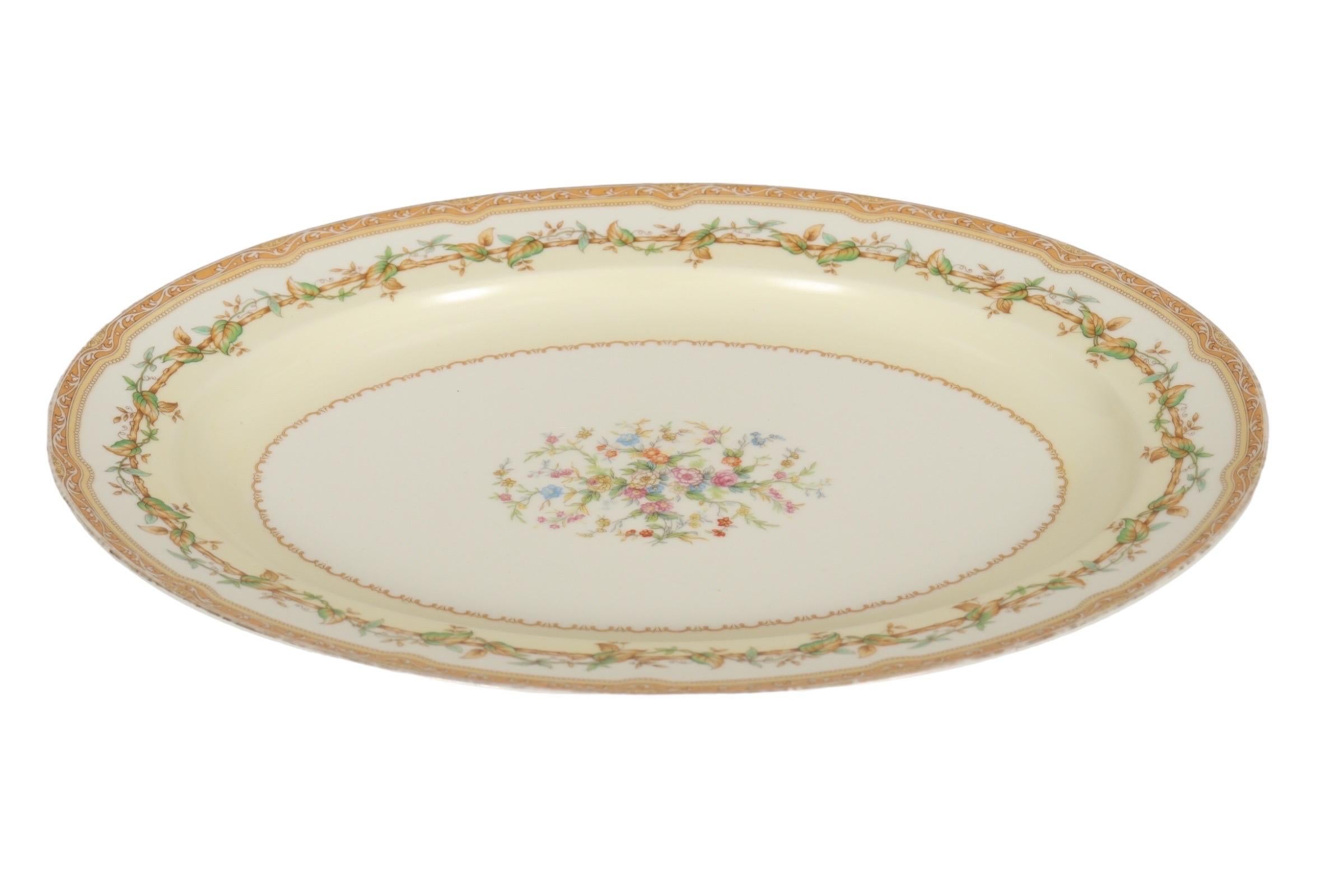 Eine Servierplatte aus japanischem Transferporzellan von Noritake mit dem Muster Olympia. In der Mitte befindet sich ein farbenfroher Blumenstrauß mit einer Weinblattbordüre in Grün und Karamell, die mit fein geprägten kleinen Blättern verziert ist.