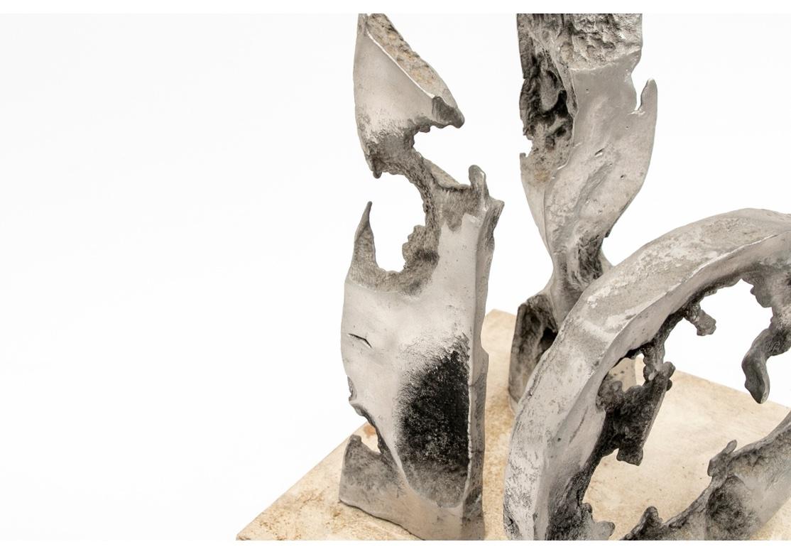 Una scultura astratta in alluminio grezza e totemica di Norma Flanagan. Firmato sul fondo di un pezzo piatto. Una composizione con due pezzi astratti frastagliati in metallo grigio scoria e un pezzo circolare con un interno irregolare. Tutti e tre i