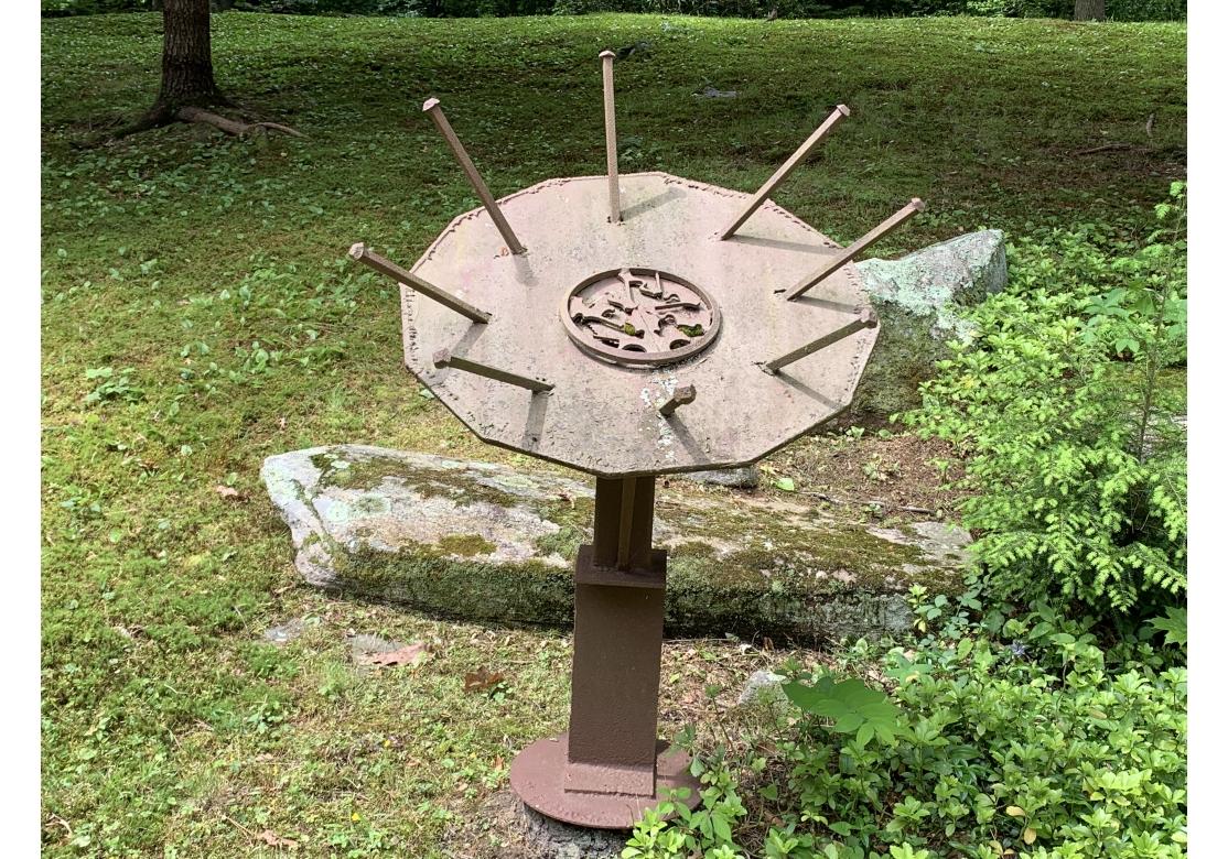 Signed on the base. The steel sculpture originally painted, now worn to bare metal with a rust patina. A large circle with an abstract decorated center in relief, the whole set at an angle with projecting spikes on a pedestal. With curved supports