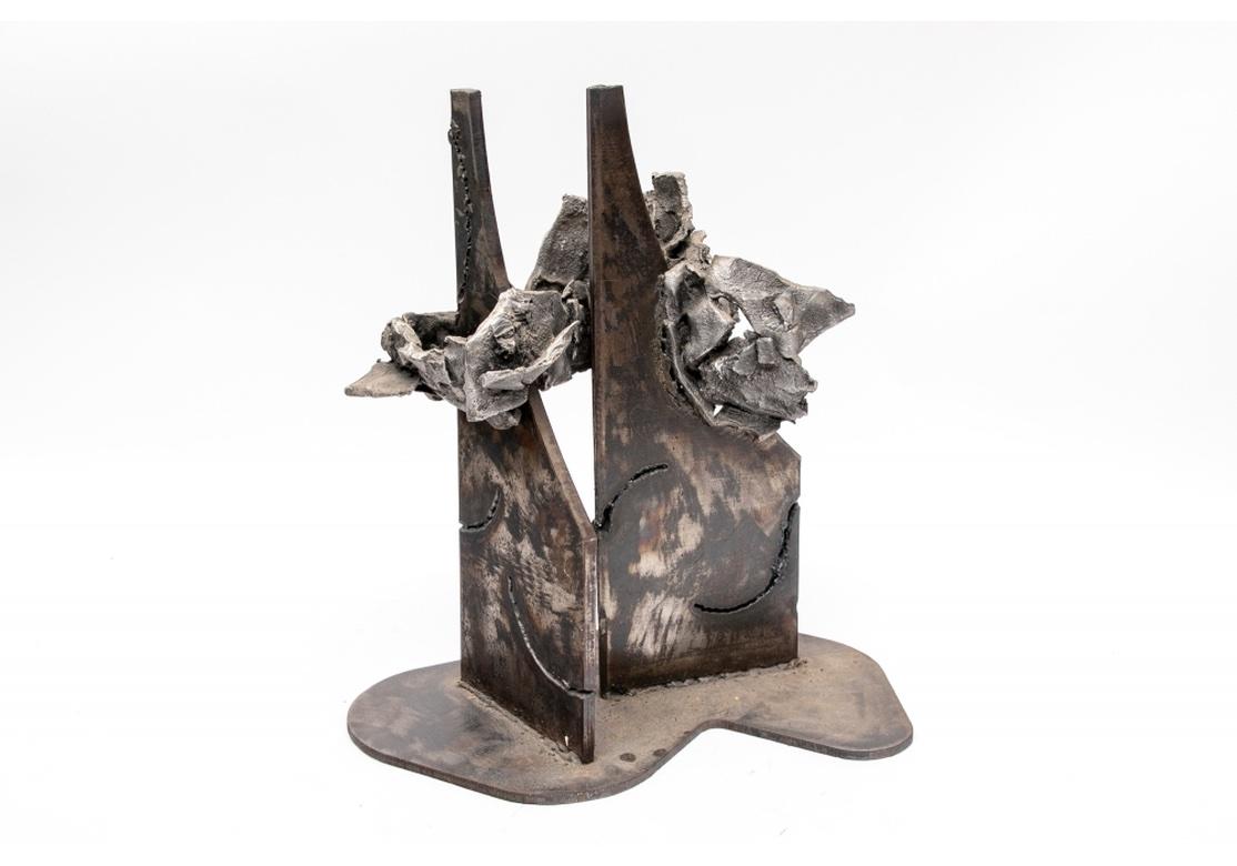A raw and powerful sculpture by Norma Flanagan. The Abstract form with two tall dark metal pieces in the center with attached irregular shaped cast gray slag metal pieces. The whole mounted on a shaped metal base. The noted Multidisciplinary CT