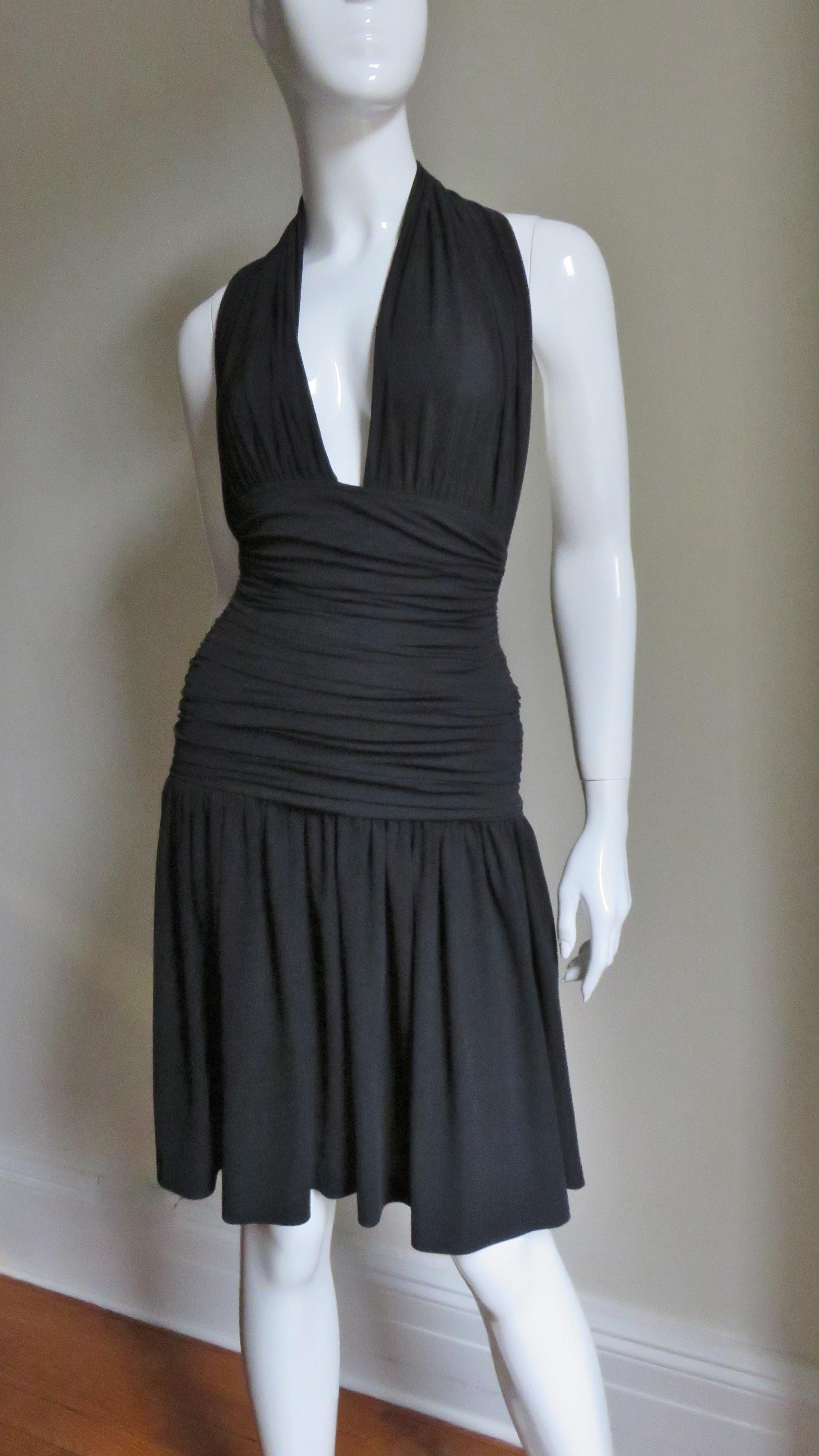 A great black jersey halter dress by Norma Kamali.  It has a ruched plunging halter neck and a horizontally ruched band from under the bust through to the upper hips.  The skirt is gathered and full and the dress slips on over the head. 
Fits sizes