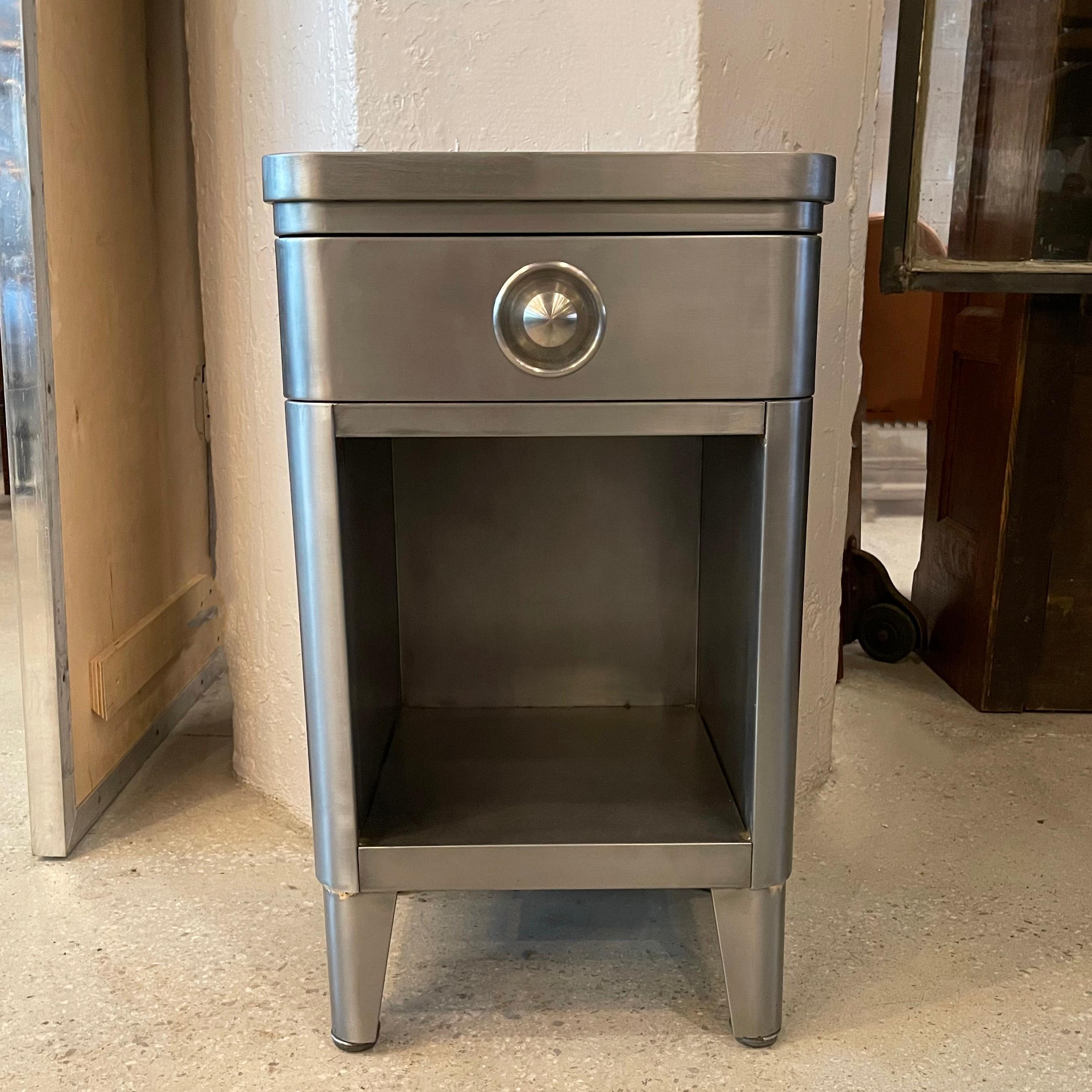 Machine-age, brushed steel nightstand or end table by Norman Bel Geddes for Simmons Company Furniture features a 3 inch height, top drawer and 13 inch, open storage below.