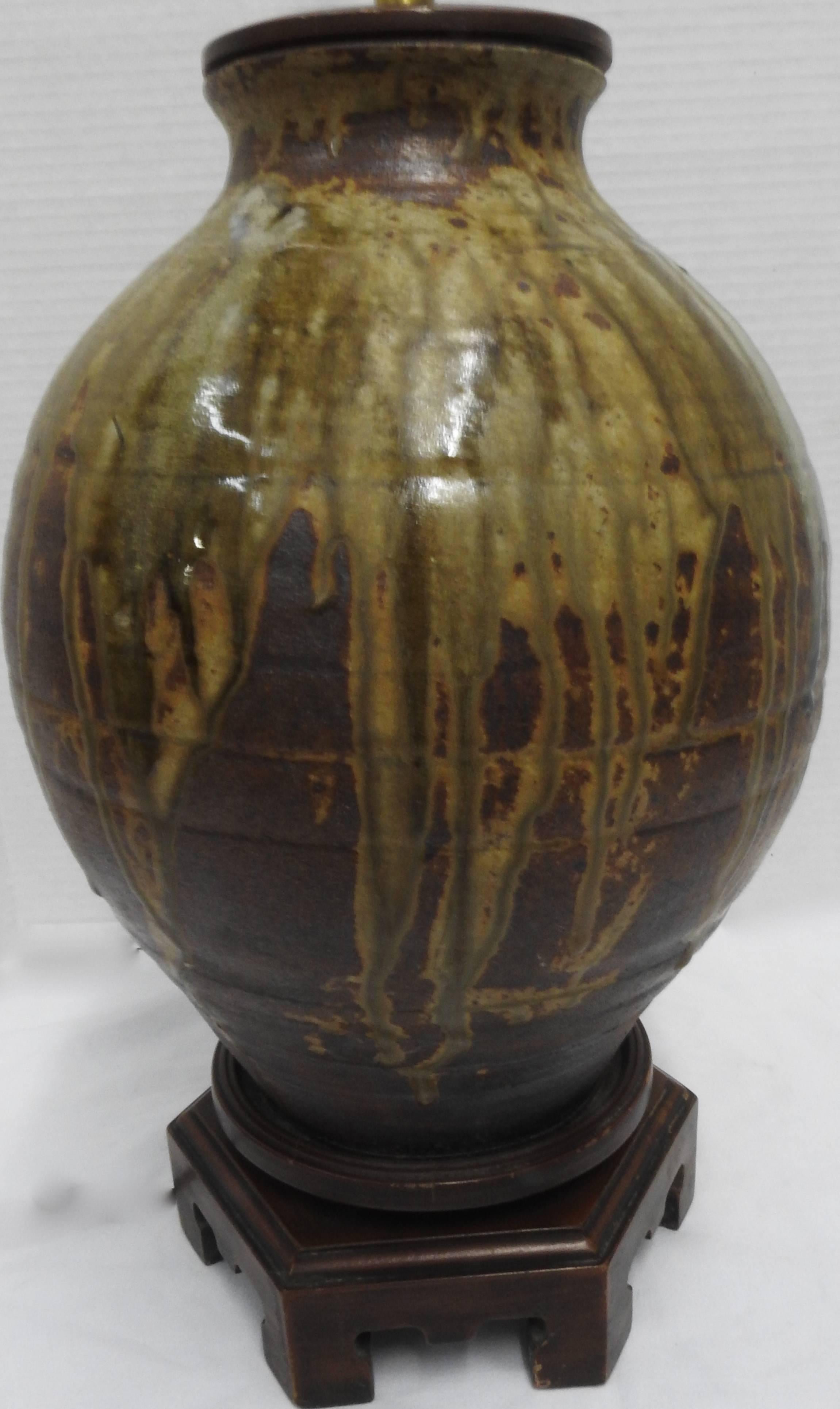 This is a stunning Norman Perry, Inc. lamp with a rich art pottery body with wood cap and base, circa 1970. Streaks of green and gold enliven the richly textured brown pottery. The top column is made of brass. The body is 17