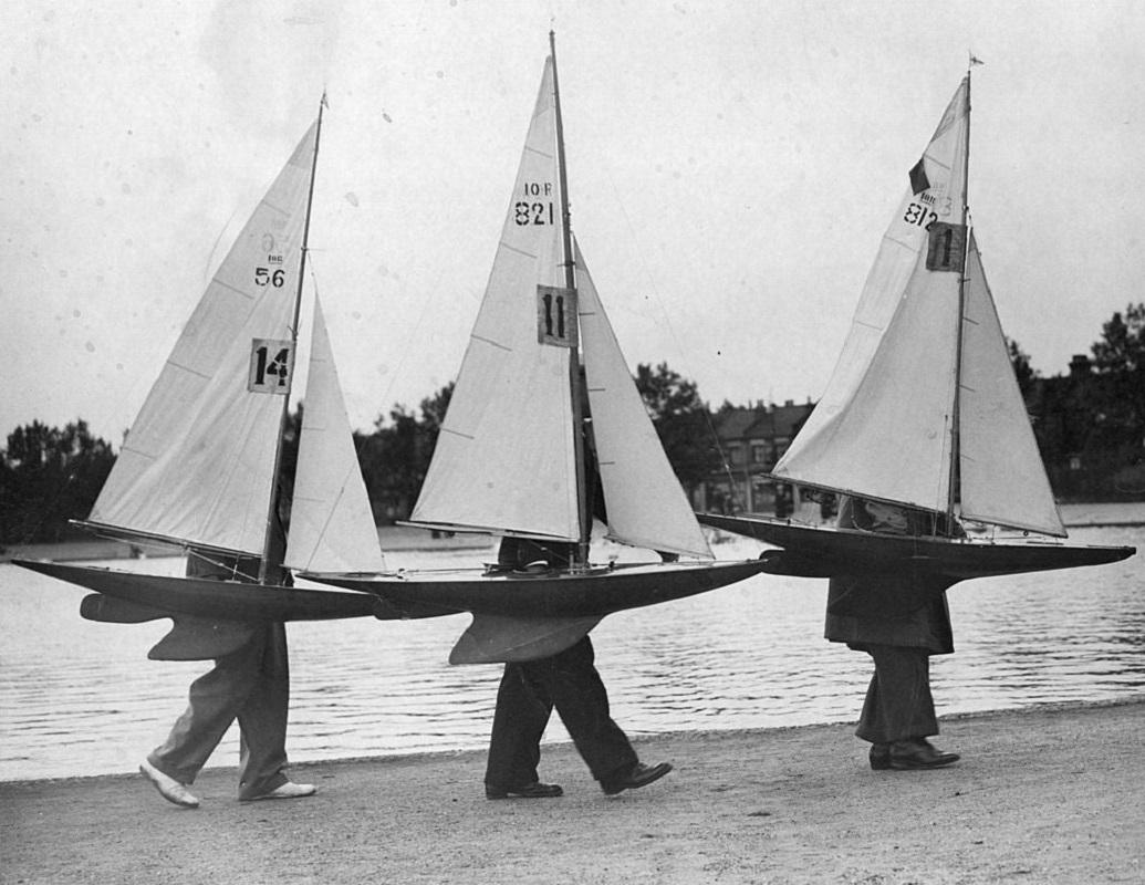 "Model Boats" by Norman Smith

20th June 1937: Three competitors for the 'Scrutton' Medals carrying their model sailing boats to the starting point at the Forest Gate Yachting Lake.

Unframed
Paper Size: 20" x 24'' (inches)
Printed 2022 
Silver