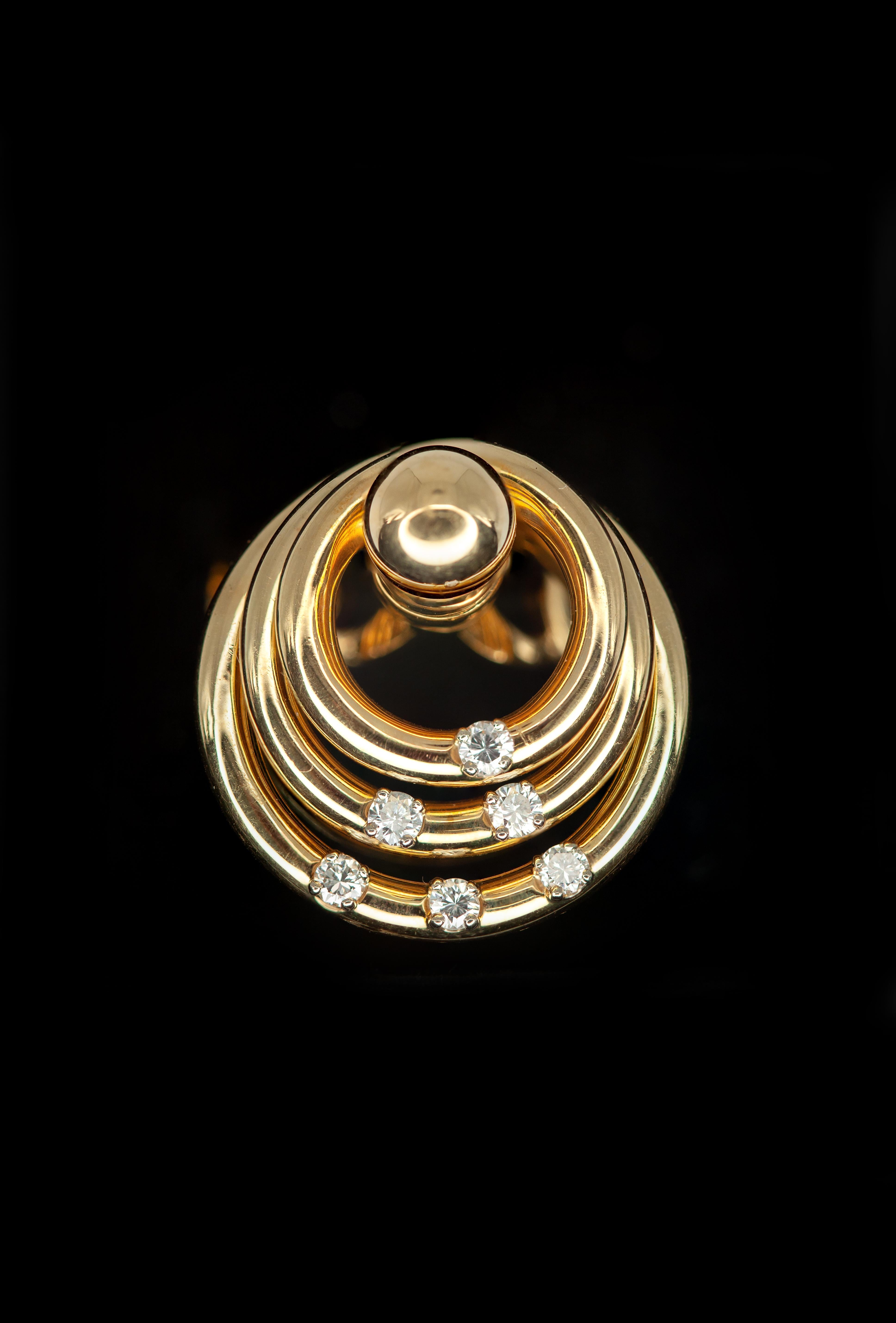 Une bague emblématique en diamant de Norman TEUFEL, réalisée en or jaune 18 carats et datée ©1972. Le design présente de multiples bandes circulaires entrelacées, rehaussées de 6 diamants taille brillant (environ 0,25 carat de couleur F-G et de