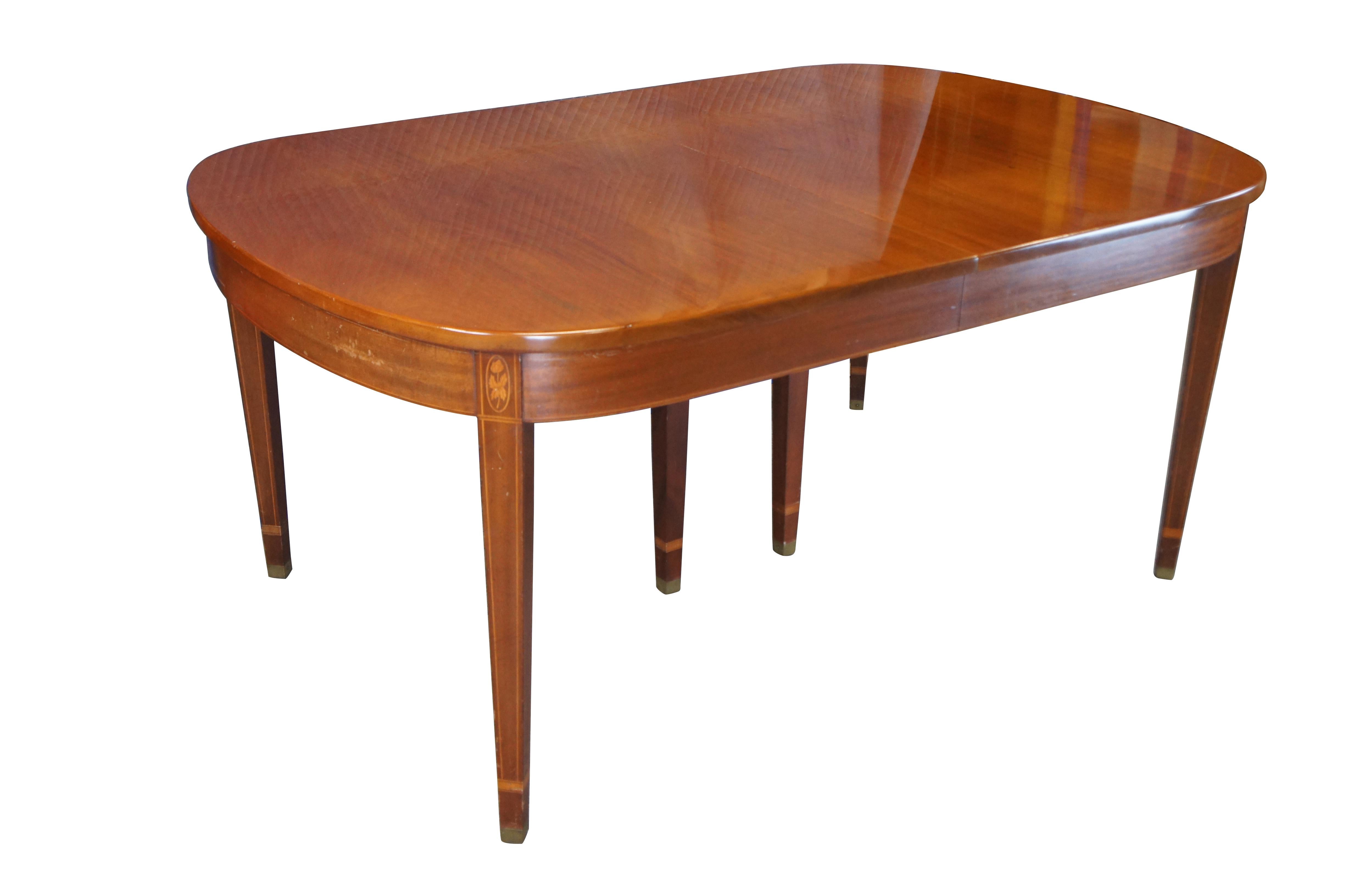 Mid-century English Chippendale / Georgian-style dining table by Norris Reproductions of Richmond, Virginia. Made from mahogany featuring oval form with inlaid banding, floral medallions, and brass-capped feet.  Leaves store inside the table for
