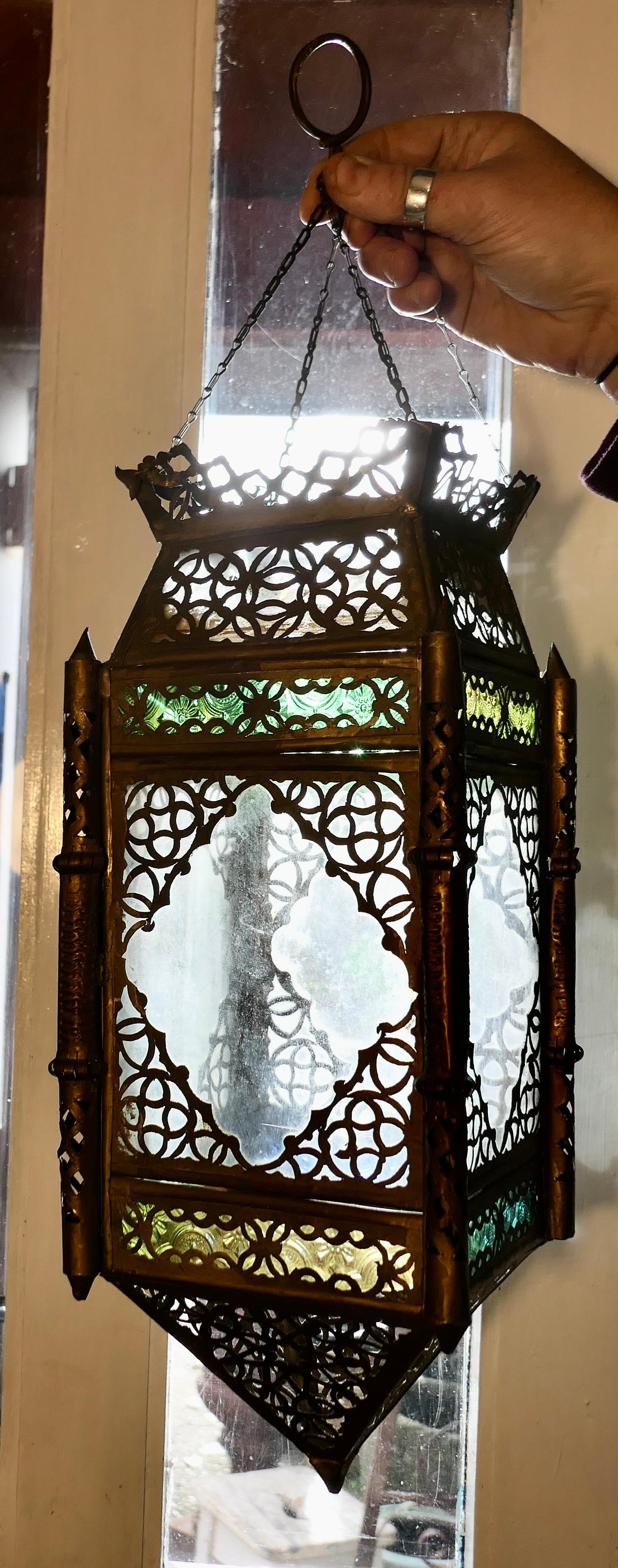 North African stained glass and brass hanging lantern shade

This is a lovely piece, it is rectangular in shape with diamond glass panels decorated with filigree brass work and small stained glass panels in Amber and Green. The lantern hangs on