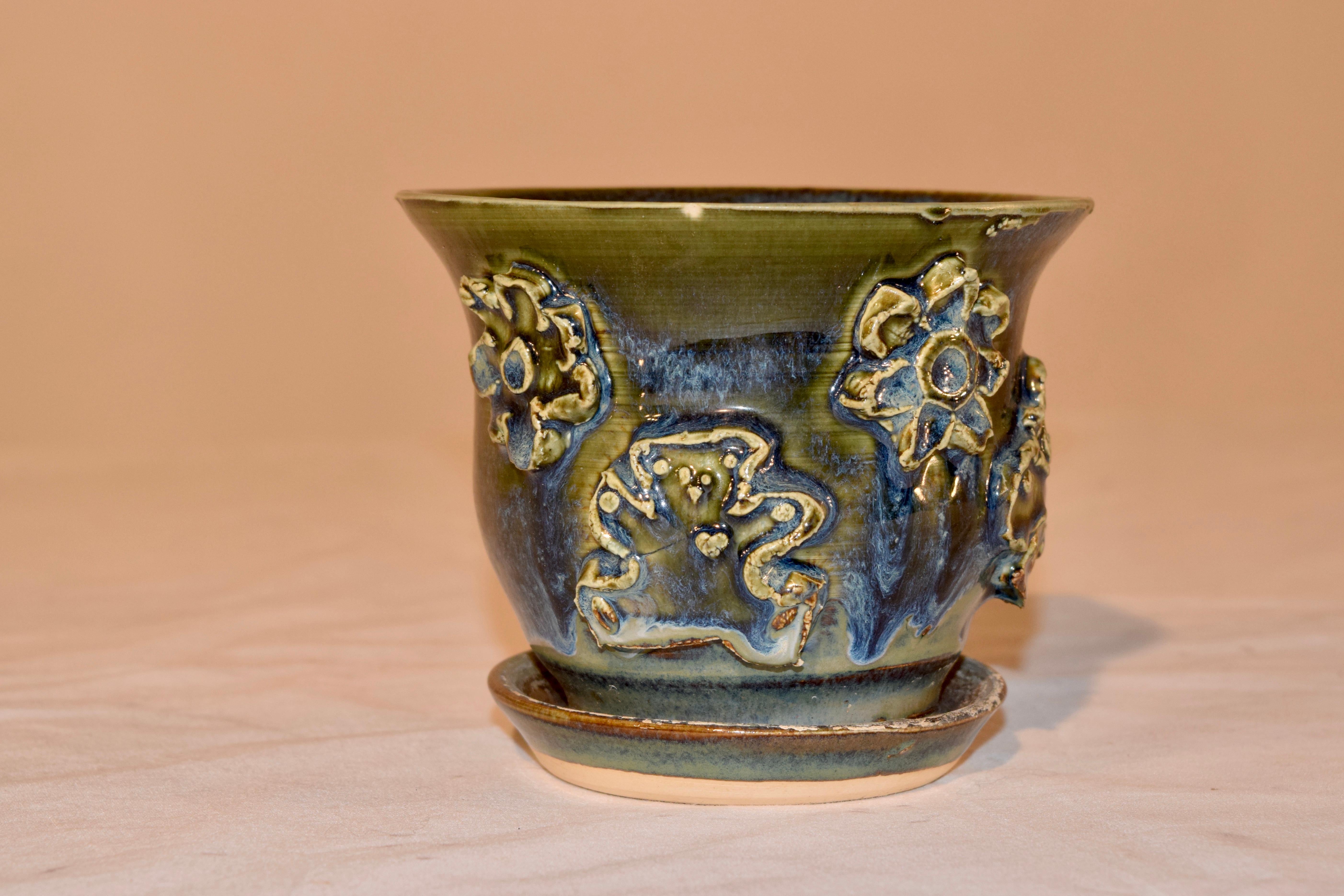 Handmade pottery flower pot from North Carolina mountains with an attached saucer. The pot has applied florals, a butterfly, and a bear. Lovely glaze colors.