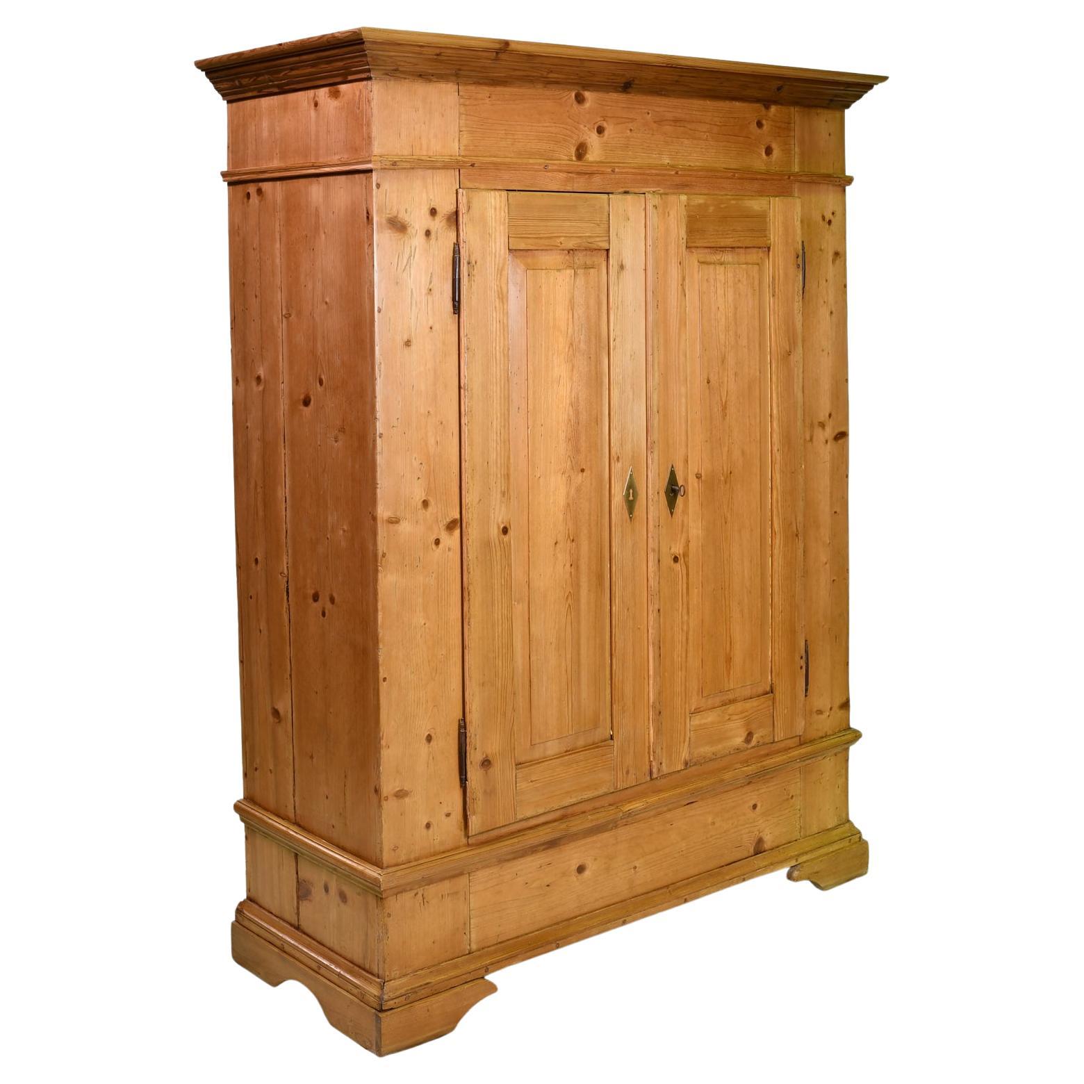 A charming antique European pine armoire with raised panels on the two doors and resting on bracket feet. This country Biedermeier armoire from North Germany was 