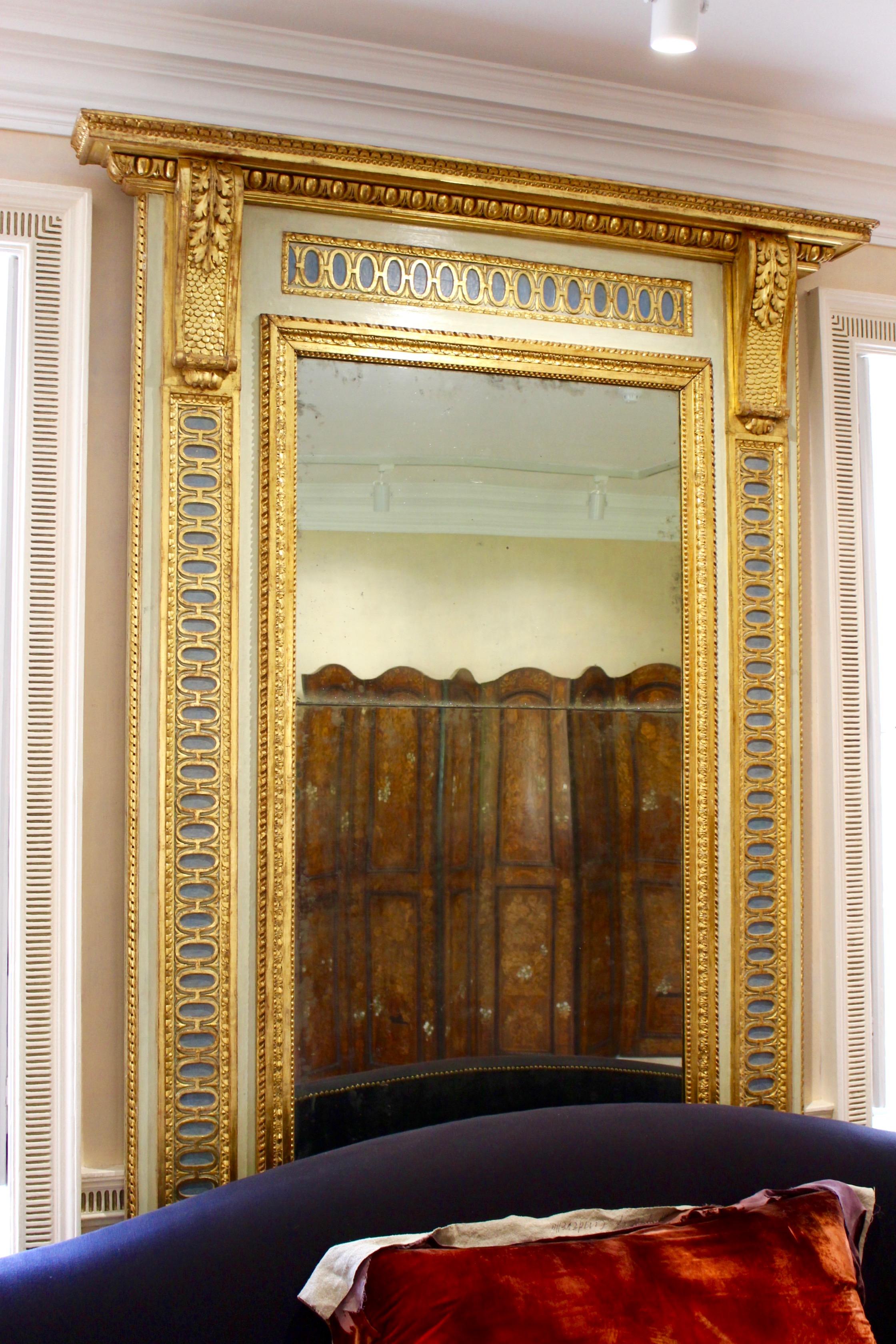 A North Italian parcel-gilt and painted pier mirror, Lombardy, late 18th century with cream and blue paint, the rectangular glass plate within a carved foliate slip and outer border with ovoid motif, the side pilasters with foliate scroll corbels.