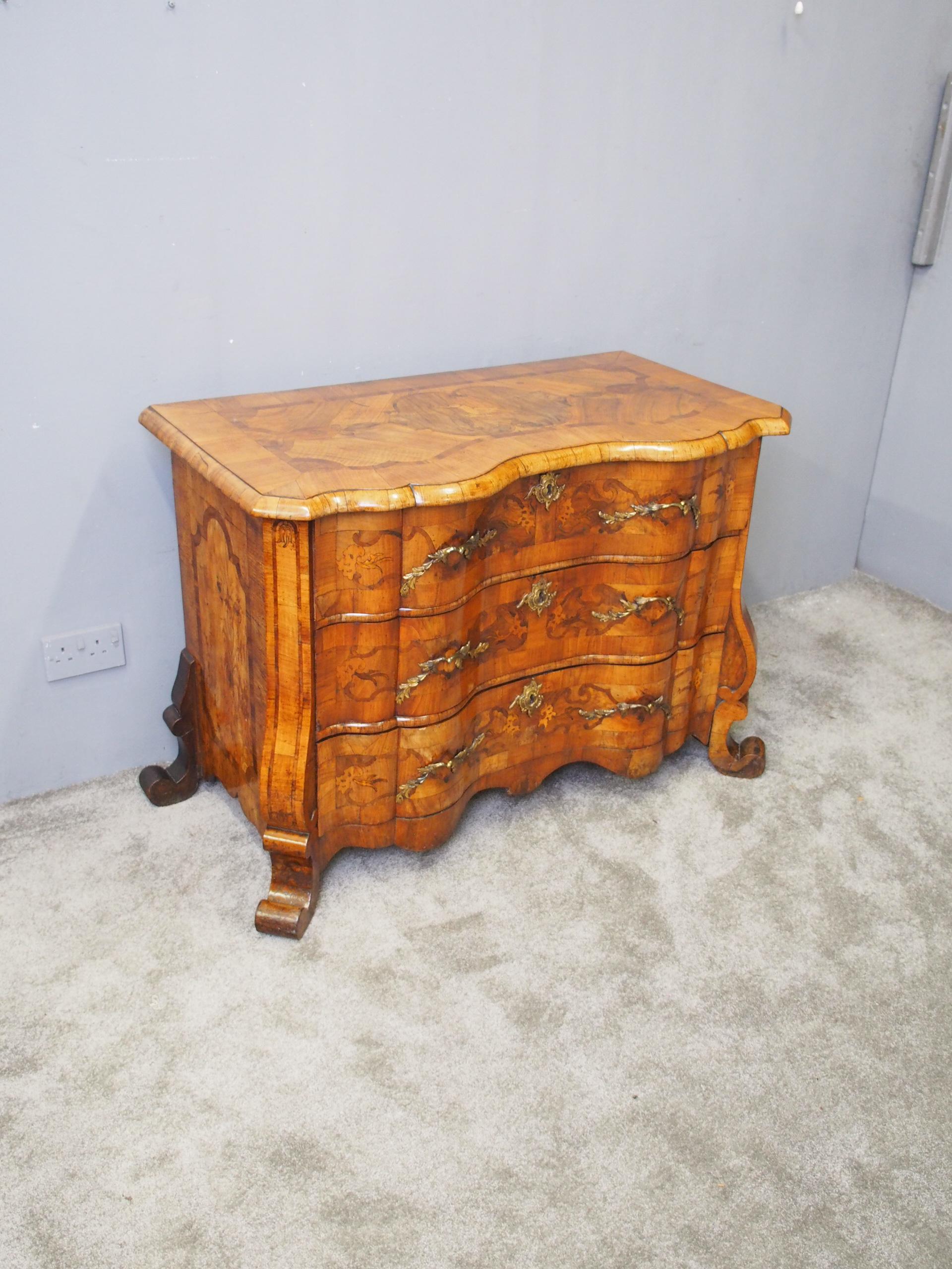 Neat sized walnut serpentine front North Italian commode. The shaped top has cross banded sections to the centre, inlaid with a mythical bird design and a half round molded edge. Beneath is a configuration of 3 shaped drawers, inlaid with various