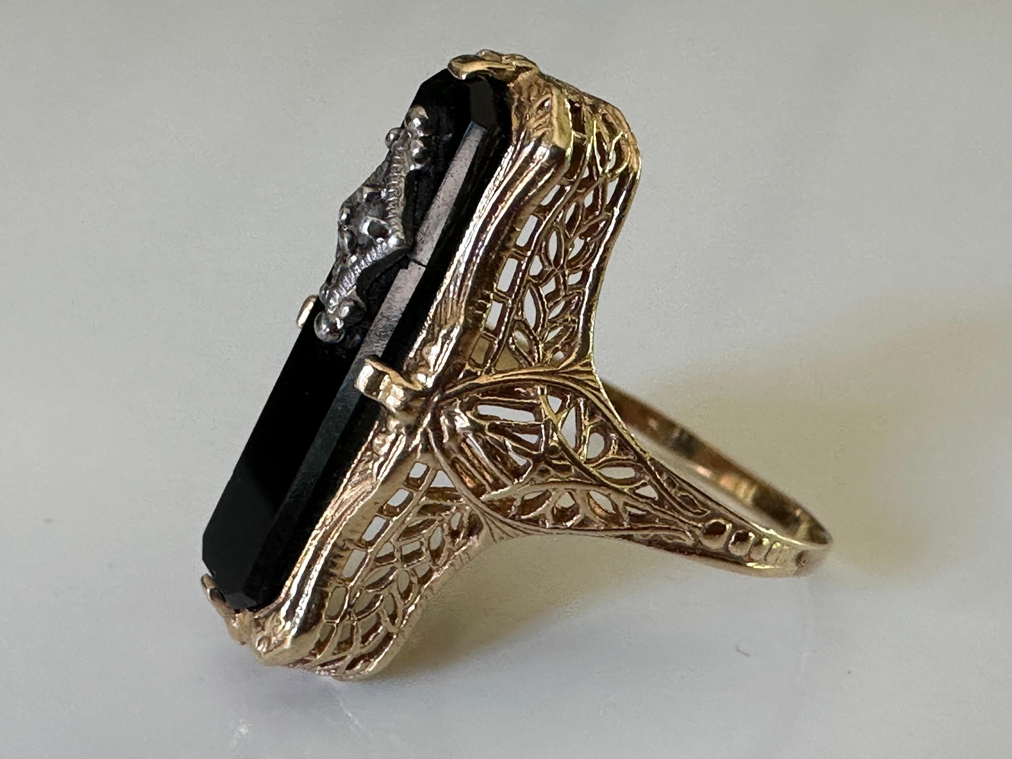 Crafted in the 1940s, this North-South ring features a round brilliant-cut diamond measuring 0.01 carats glistening from within an onyx plaque and fine filigree details. Set in 14K yellow gold. 