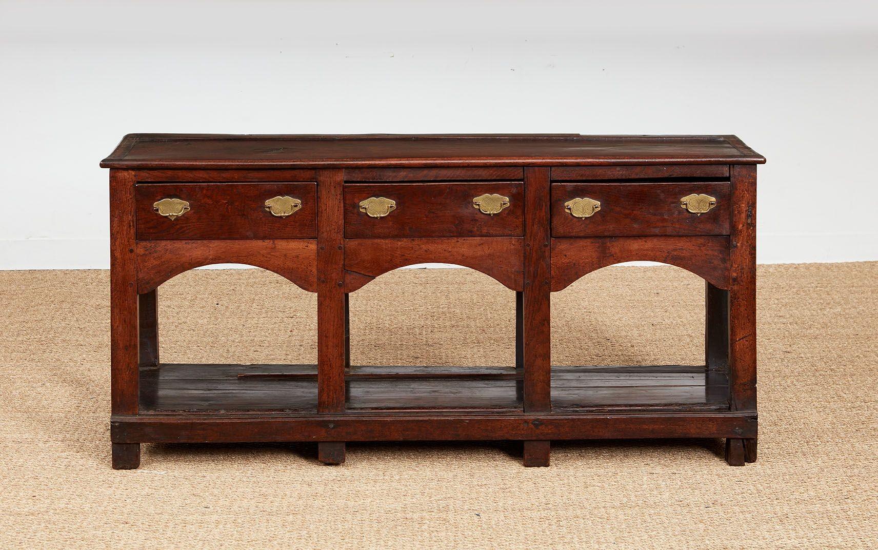 A North Wales dresser base or sideboard having thick single board top with rounded edges over three drawers each with double bail pulls with etched escutcheons over an apron with three arches, standing on eight substantial square section legs, with