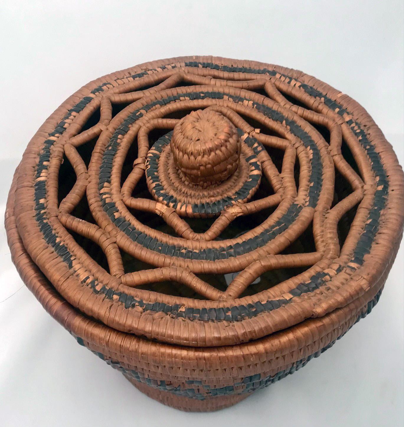 The Salish basket, circa 1900, is finely woven with a stylized imbricate design, the cover has a cutout star design with central knob, there are minor losses to the decoration, particularly to the cover.