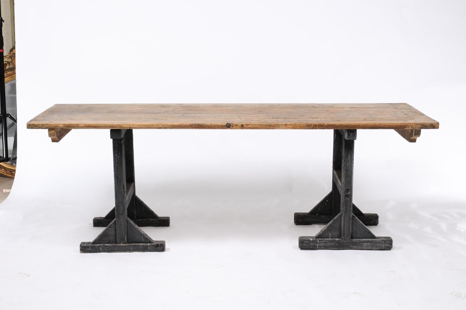 A French long pine work table from the early 20th century, with black-painted trestle base and rustic rectangular top. A sturdy and nicely rustic work table from Northern France. Made of pine, the plateau has an aged patina and loads of character.