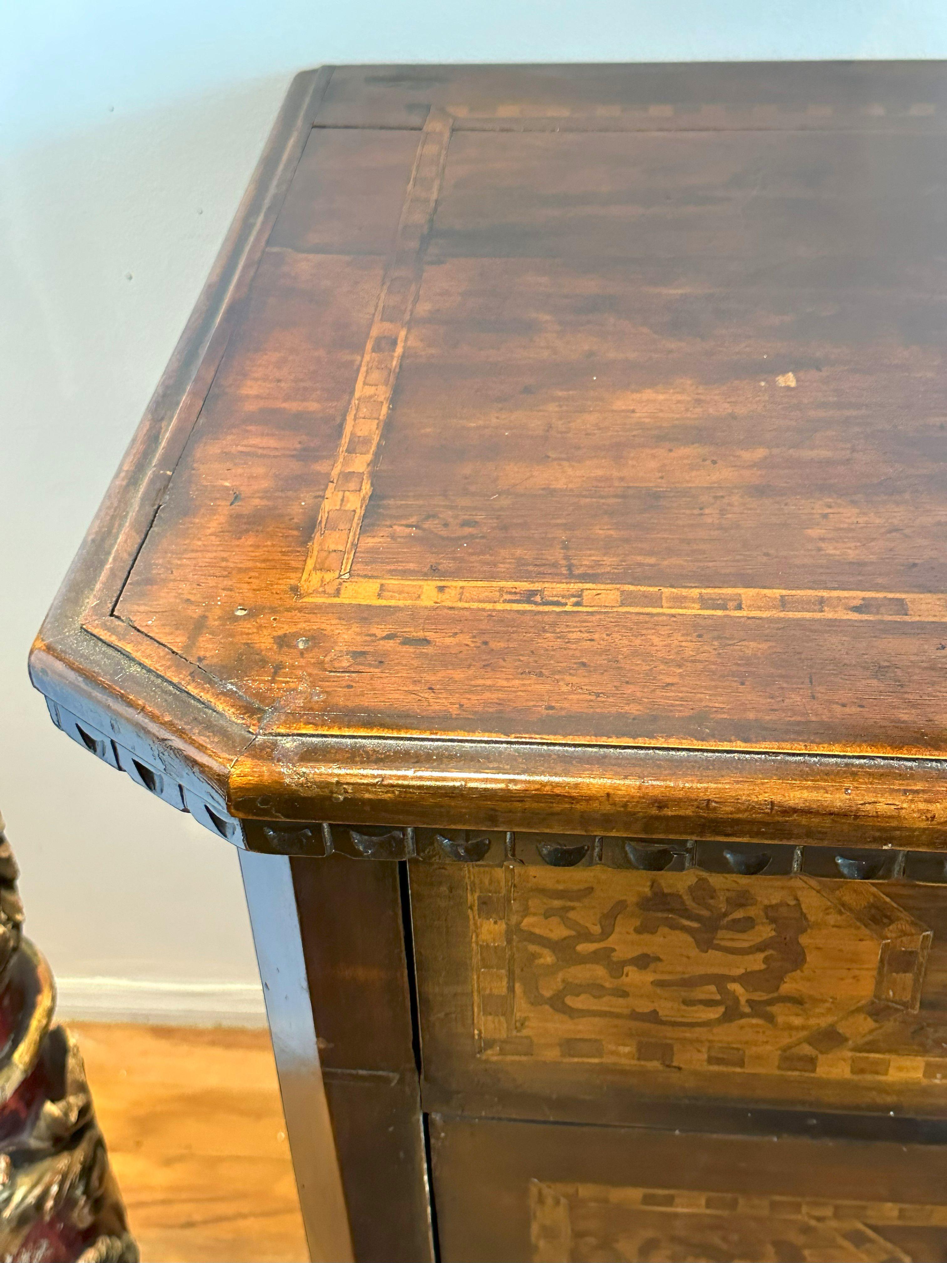 The rectangular inlaid top with canted angles and a shallow chip carved frieze. Conforming case fitted with three inlaid drawers raised on bracket feet. 