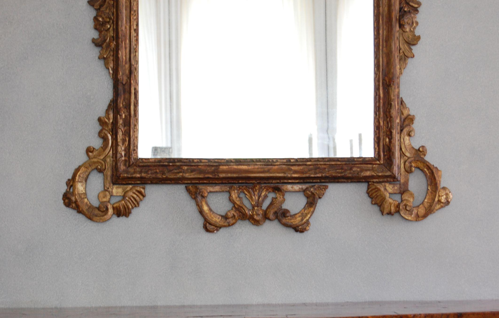A northern Italian giltwood mirror surmounted by a further flower decorated plate and floral clasp, surrounded by C- scroll and foliate borders. Center glass is a 19th century replacement. Very good overall condition.