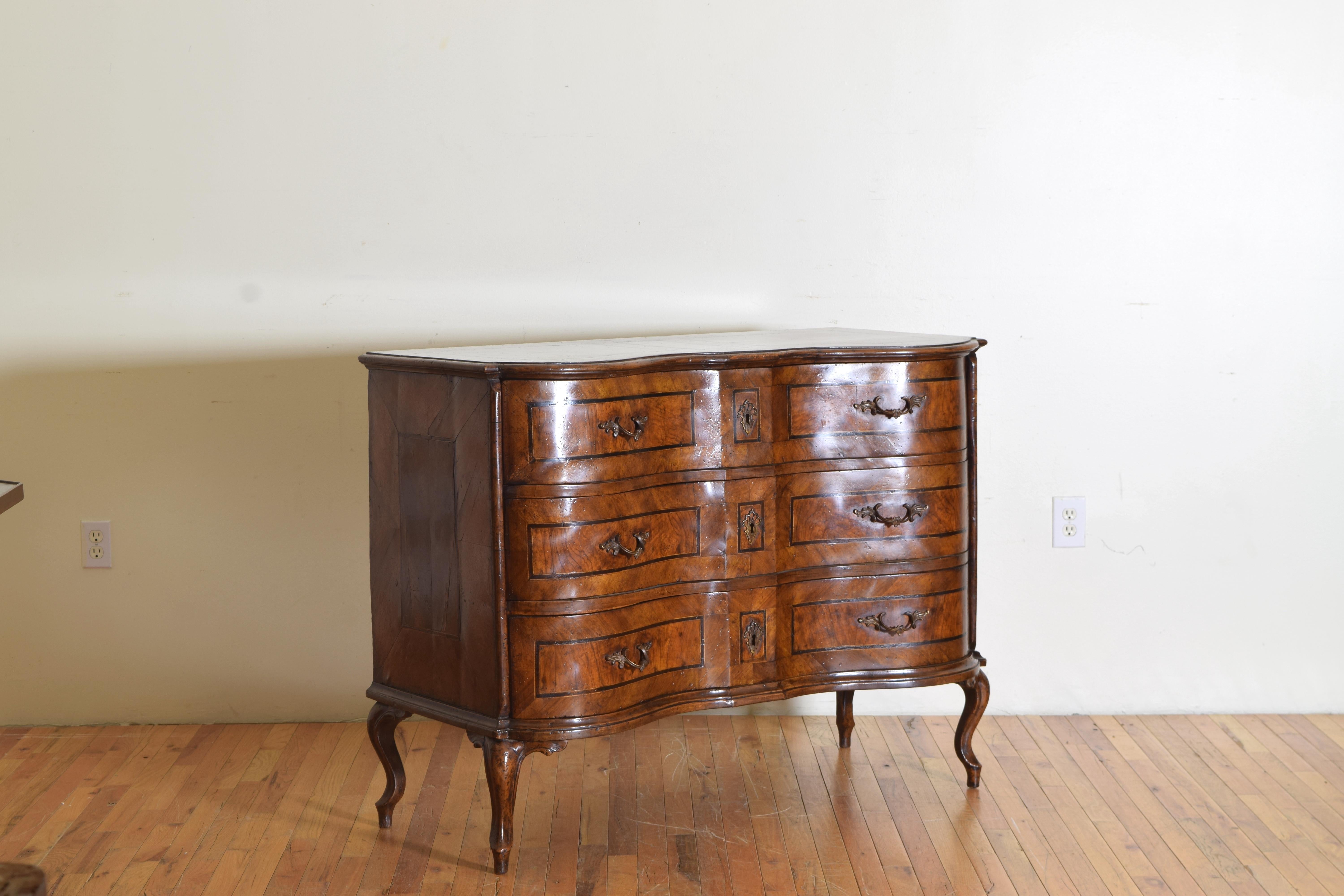 Finely crafted, the shaped top, a cross between a bow front and a serpentine front with an inlaid patterned border within a ground of beautiful burl walnut veneer, the conforming case housing three drawers all with patterned inlay and burl walnut