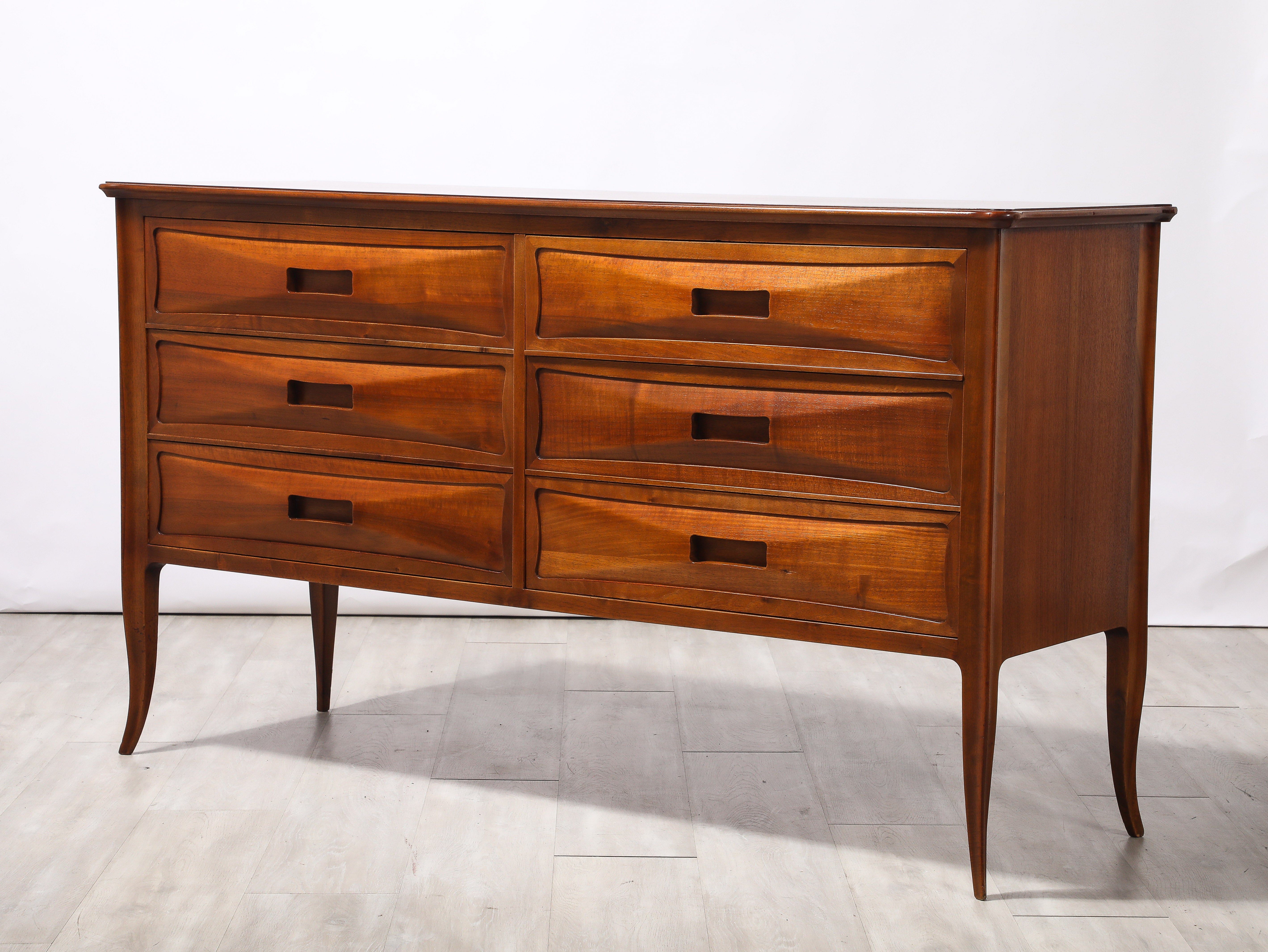 Cassettiera / credenza in noce del Nord Italia intagliata a mano; la superficie rettangolare poggia su sei cassetti orizzontali, due affiancati su tre livelli. I cassetti frontali ad arco con eleganti maniglie a taglio orizzontale sono sostenuti da