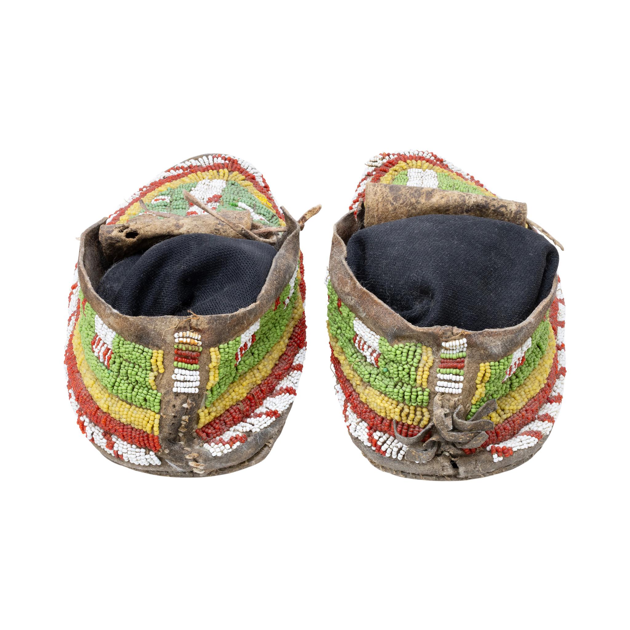 Native American Northern Plains Indian beaded moccasins with buffalo hoof design. Sinew sewn on green background with greasy yellow, red and white designs. Great patina on beadwork and leather. Would display nicely in a Southwestern style home or