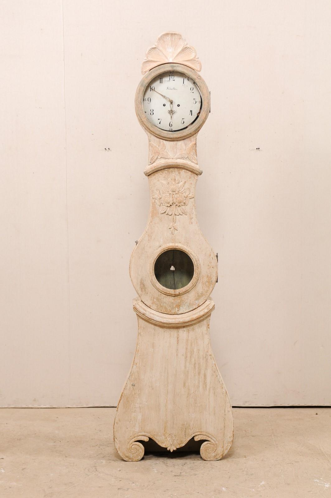 A 19th century Swedish wooden floor clock. This tall antique clock from northern Sweden features a raised bonnet of fanned leaves at it's top, and decorated with foliage and floral bouquet about the neck and upper chest. There is trim molding which