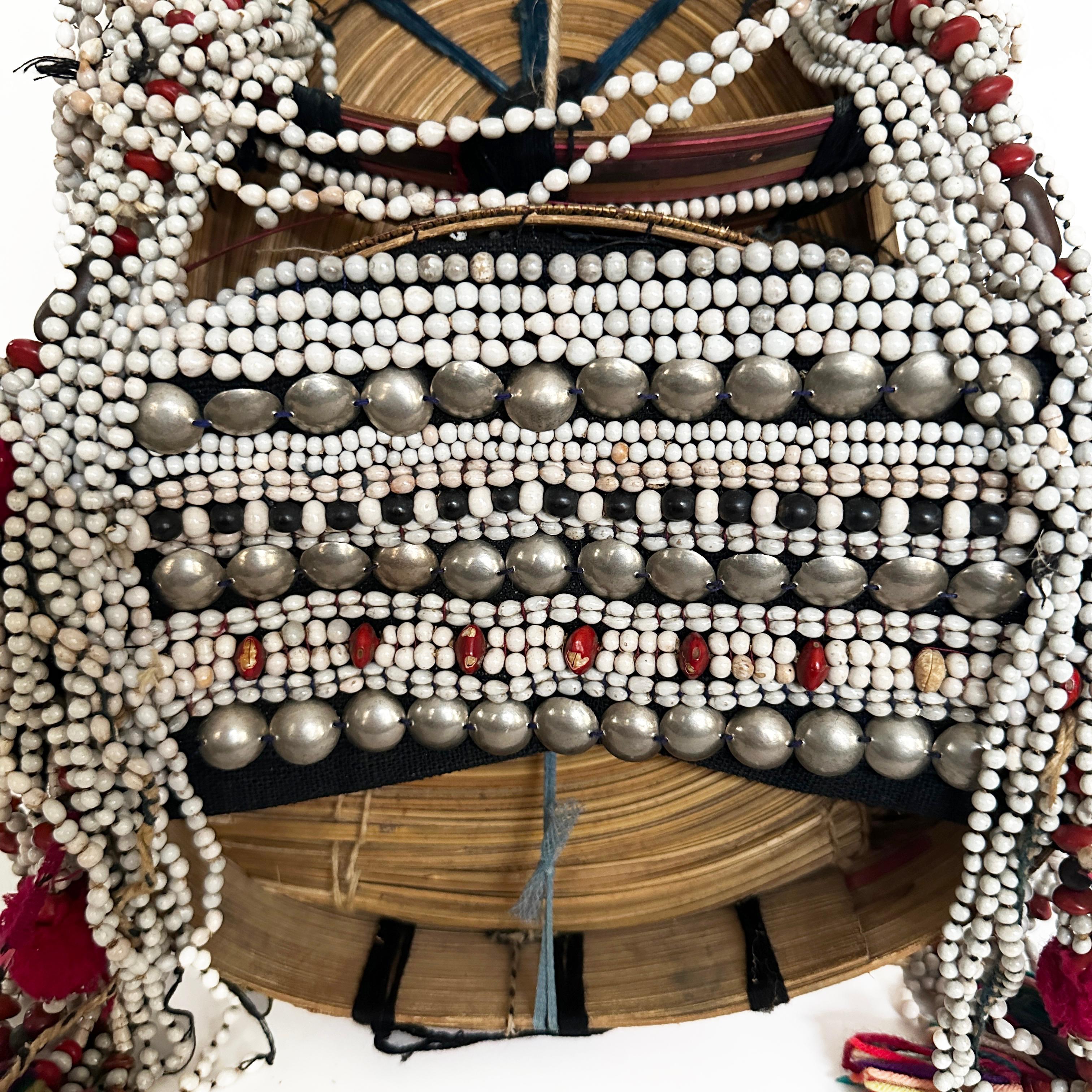 Coiffe tribale d'une femme Ulo Akha faite d'une armature de bambou et ornée de perles, de pompons, de graines et d'autres objets uniques. Cette pièce offre un aperçu de la riche tapisserie culturelle du nord de la Thaïlande et de l'art et des