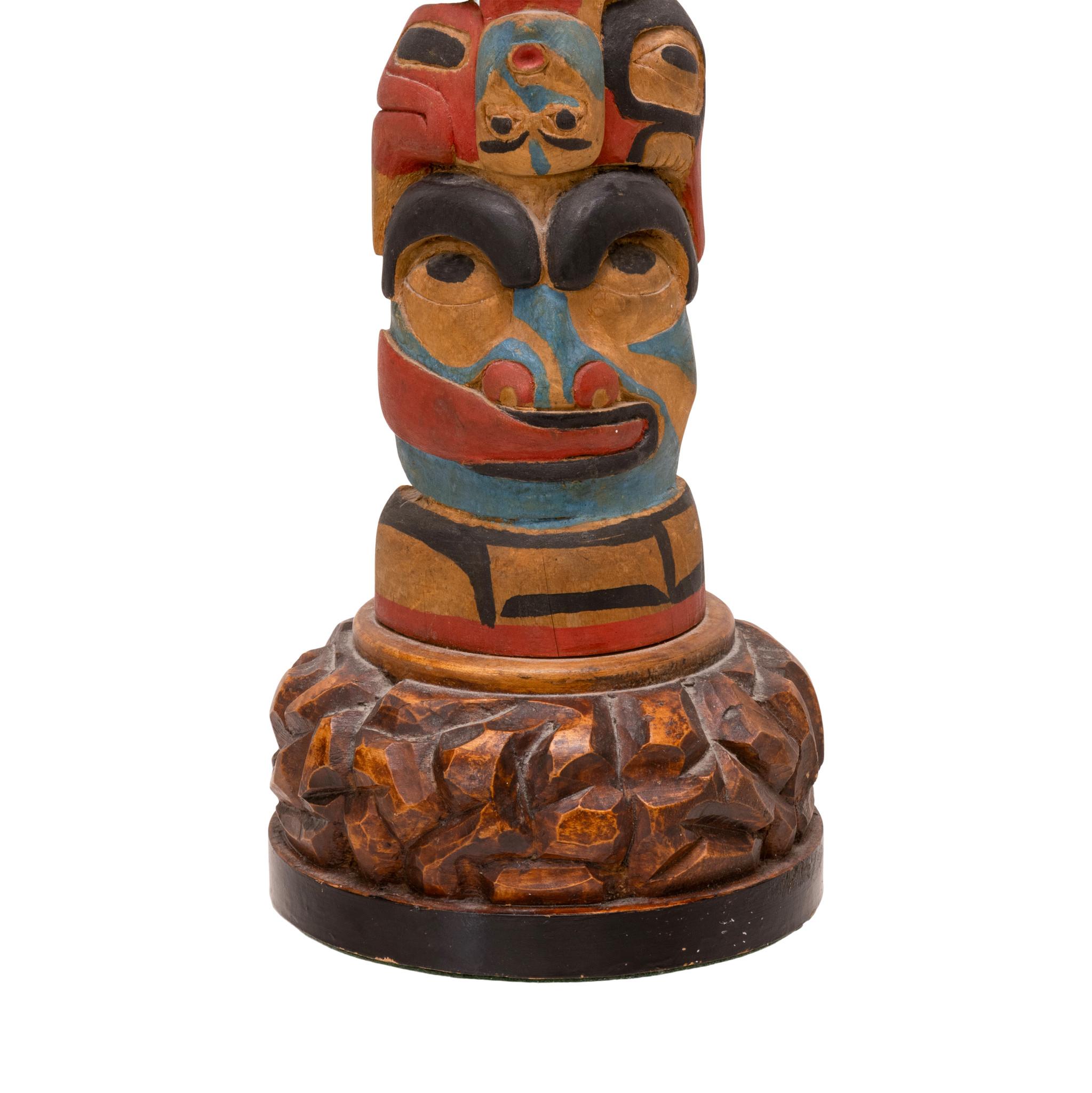 Northwest Coast Bella Bella totem pole. Portraying three finely carved masks above a bear with elongated tongue wrapping around face. Painted in colors of red, blue and black on natural wood. Unique carved base. Stunning piece for display in a