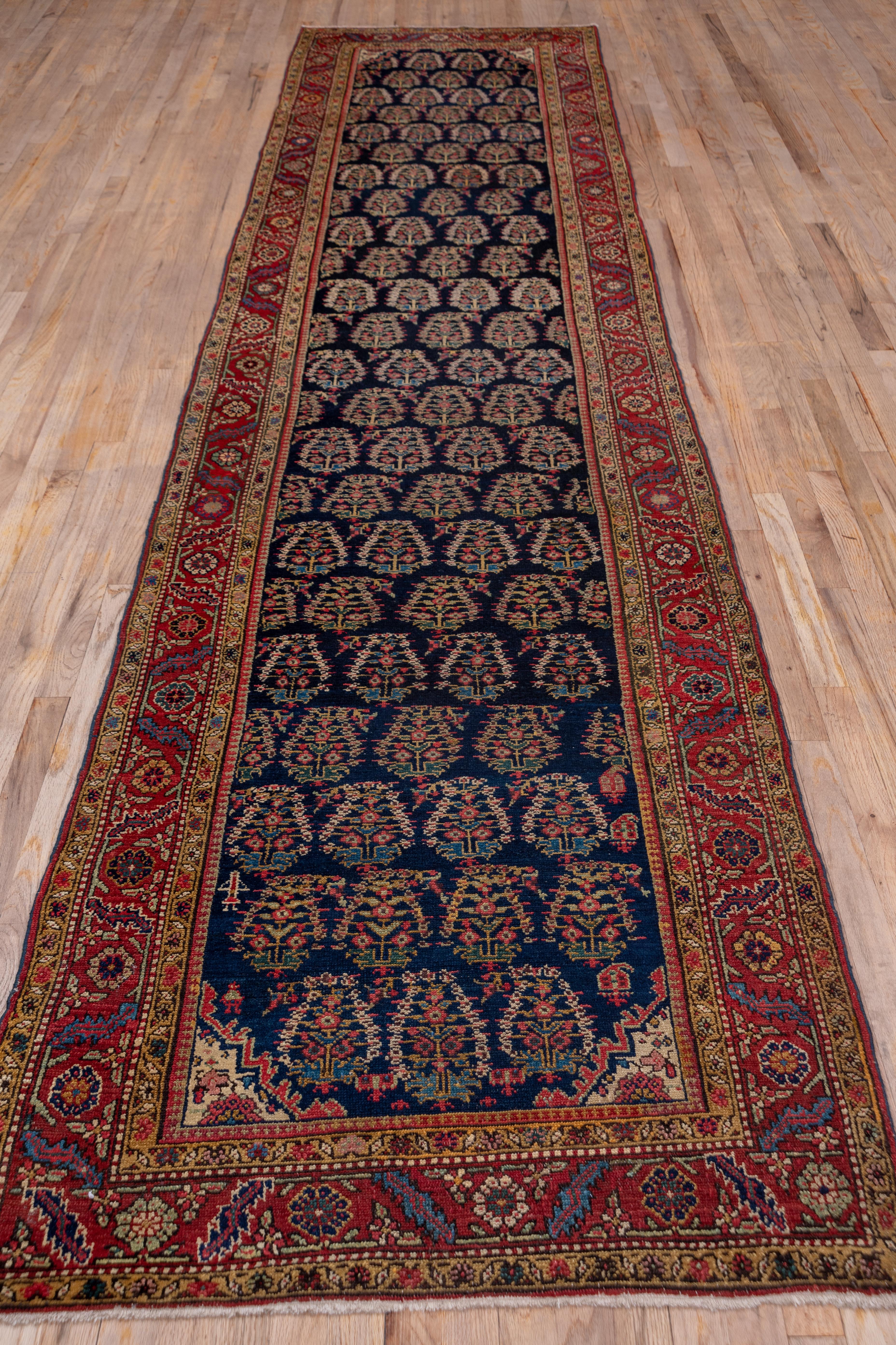 The rich navy field of this rustic Azerbaijani runner displays an offset pattern of row-b-row reversing floriated botehs, with a few lesser cones and a human figure tossed in. Fractional botehs often fill out a row. The red main border employs