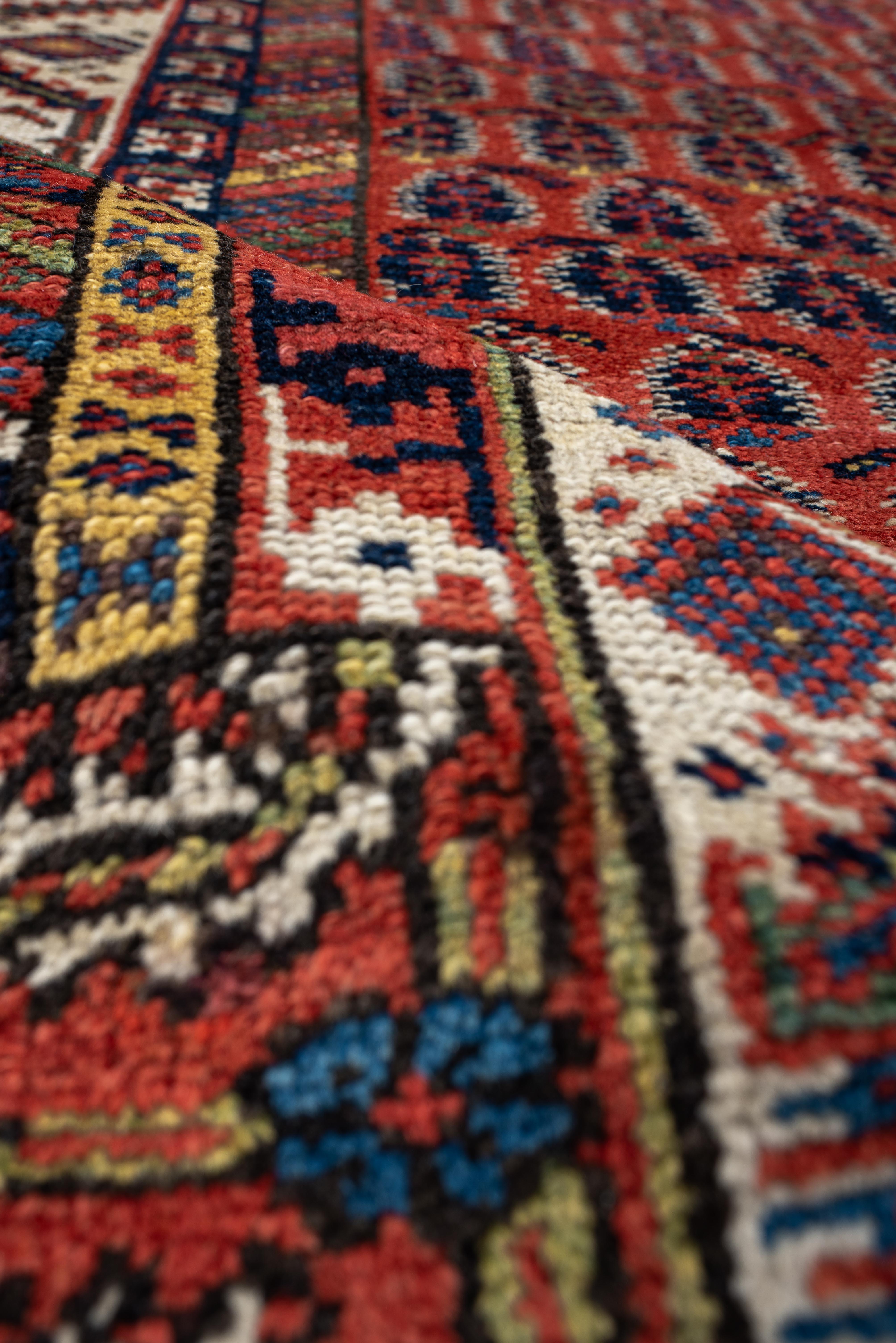 Dieser antike nordwestpersische Teppich zeigt ein rhythmisches Feld sich wiederholender Boteh-Motive - stilisierte Paisley-Formen, die oft als Symbole für Fruchtbarkeit und Wiedergeburt gelten -, die auf einem satten, ziegelroten Grund angeordnet