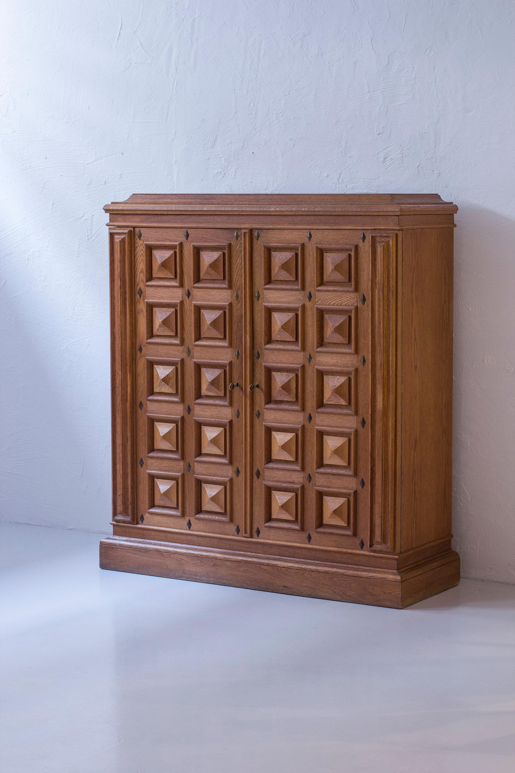 Norwegian Art Deco cabinet made during the 1920-30s. Made from oak with brass details. Heavy geometrical relief patterned doors. Two original keys made from brass. Adjustable drawer shelves on the cabinets right side. Good vintage condition with