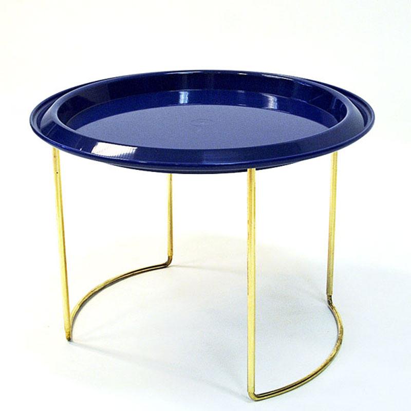Beautiful Norwegian round tray table on a foldable brass foot designed by Herman Bongard for PLUS Norway in the 1960s. This practical little table has two removable plastic table tops. One bright blue and one light transparent grey plate. You can