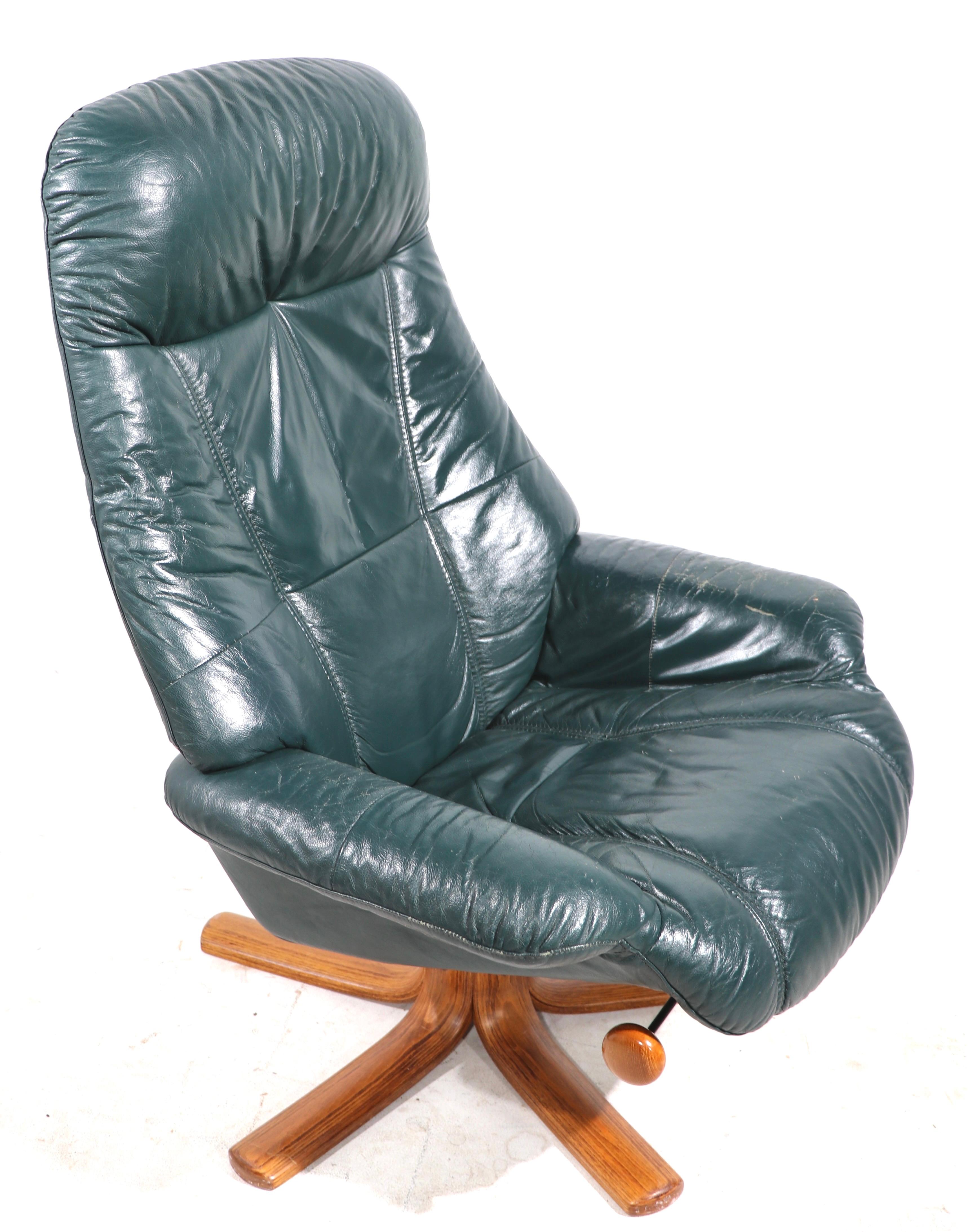Comfort, style and quality - Scandinavian Modern leather recliner with ottoman by Hjellegierde Mobler. The leather is medium dark green, the chair swivels, and the back reclines - the car and ottoman are on splay leg wooden bases. Great original