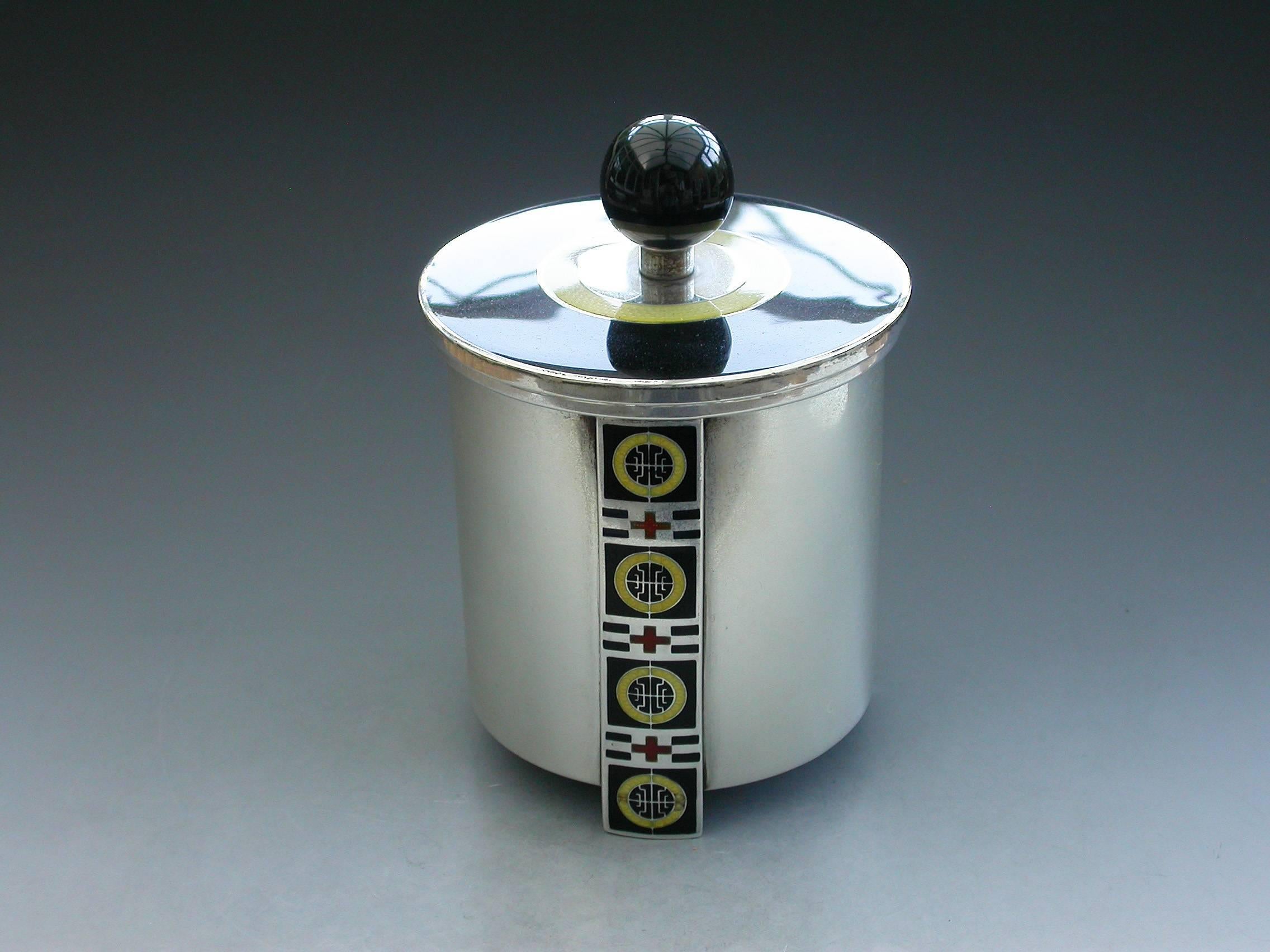 An unusual Norwegian Art Deco silver and enamel tea daddy of drum shape with three vertical supports enameled with geometric designs in black, red and yellow. The detachable cover in black enamel with a yellow band and ball finial.

By David
