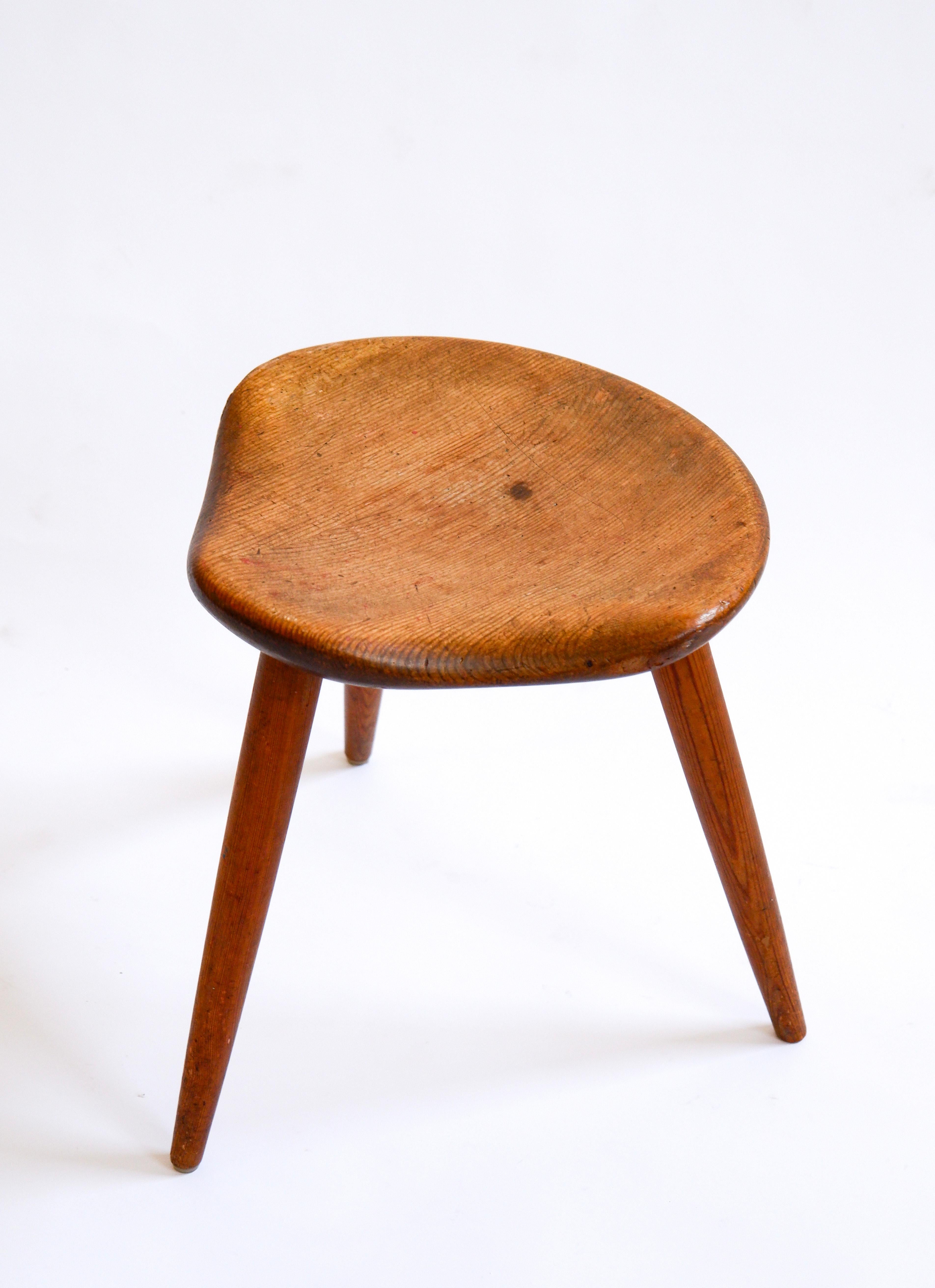 Hocker aus norwegischer Kiefer, entworfen und hergestellt von Norsk Husflid in den 50er Jahren. Dieser dreibeinige Hocker besteht aus drei schlanken Füßen mit einer Sitzfläche in Form eines Pferdesattels auf der Oberseite. Ein ganz besonderes Design