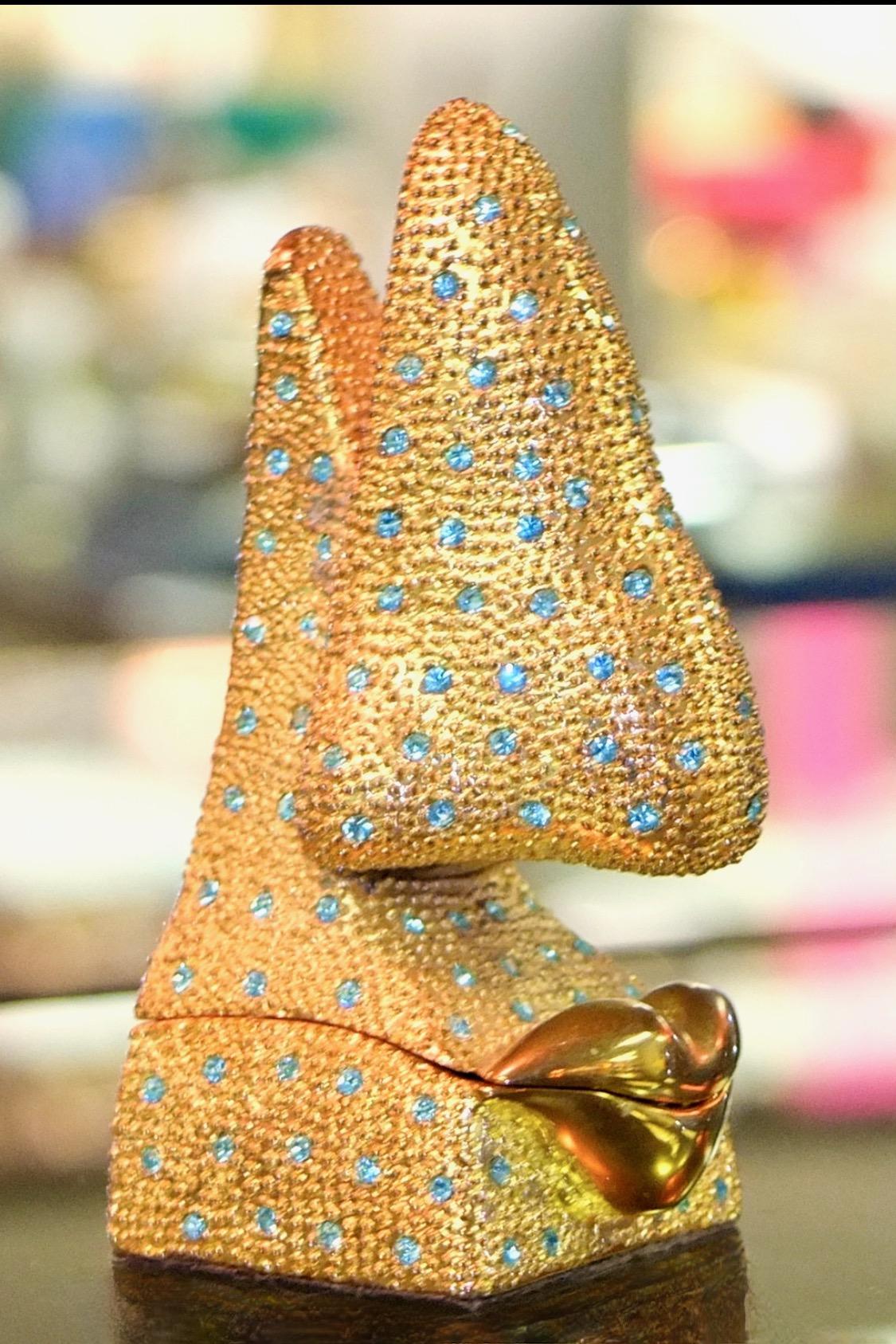 Dali-esque gilt metal snuff box bejeweled with light blue rhinestones and shaped like a surrealist human nose and lips . Magnetic closure. Yellow enameled interior. 
Amusing container for your gear. 
Capacity ~3.5 grams.
Indecipherable brand mark