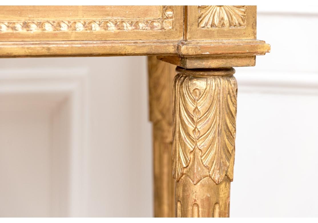 The antique French console table carved and gilt overall, the top with incurved ends and covered with an ecru damask fabric under the black conforming marble top. With an inset apron decorated with leafy bands, leaf motifs at the corners and a