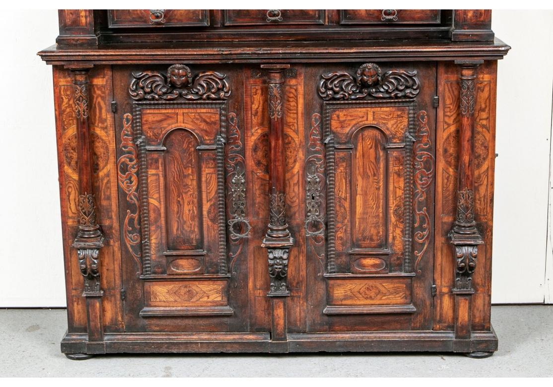 A large and impressive 17th century European cabinet. Made in two parts, both with elaborate carved decoration and burled panels and details. The upper cabinet with heavy overhanging top over dentil and burled inlaid friezes. The back with carved