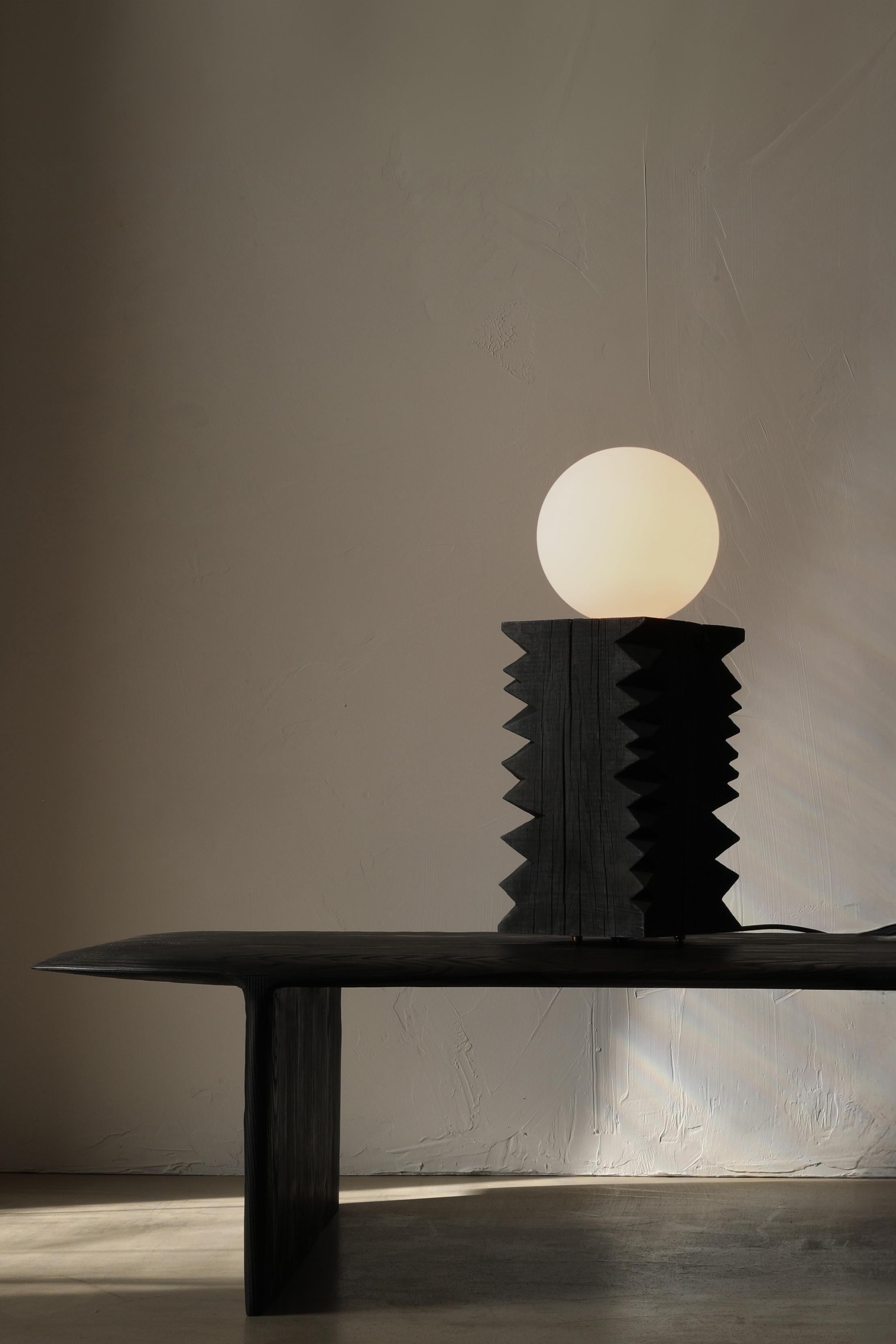 The Notch Lamp is a solid oak table lamp with a large frosted globe bulb. The lamp sits on four bronze feet and is switched on the cord with a dimmer.

This collection finds its foundation in ‘cribbage’, a rough-cut lumber used to build support